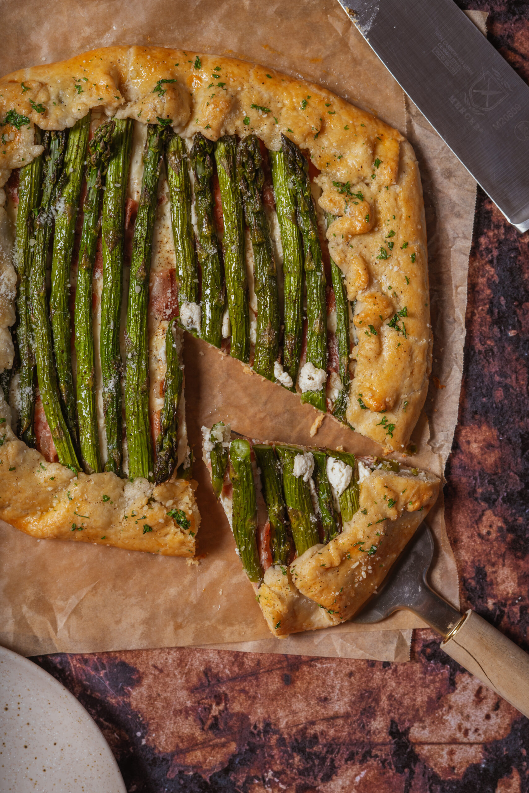 asparagus galette on parchment paper with slice taken out.