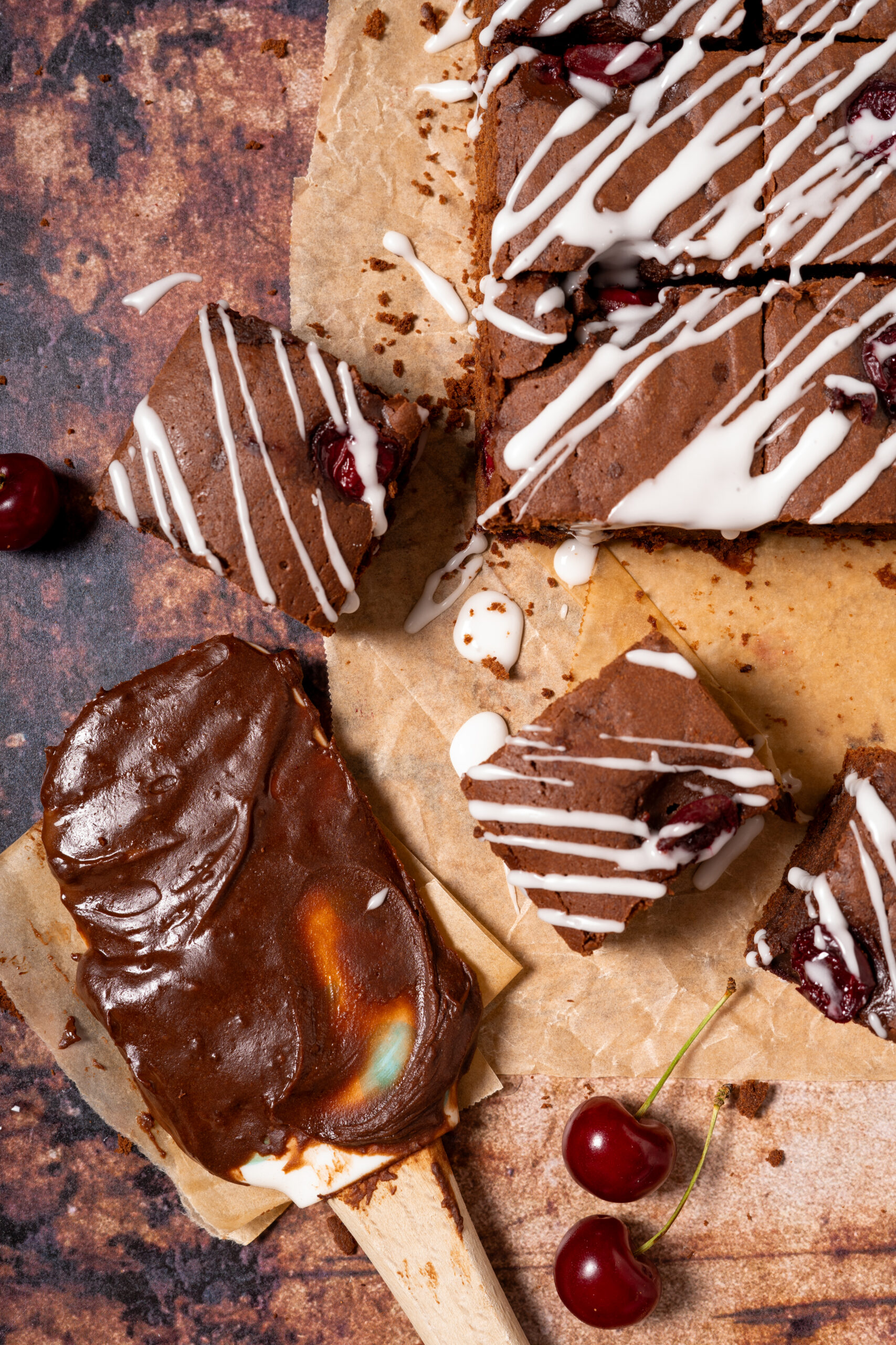 chocolate cherry brownies scattered on parchment paper with a spatula covered in brownie batter.