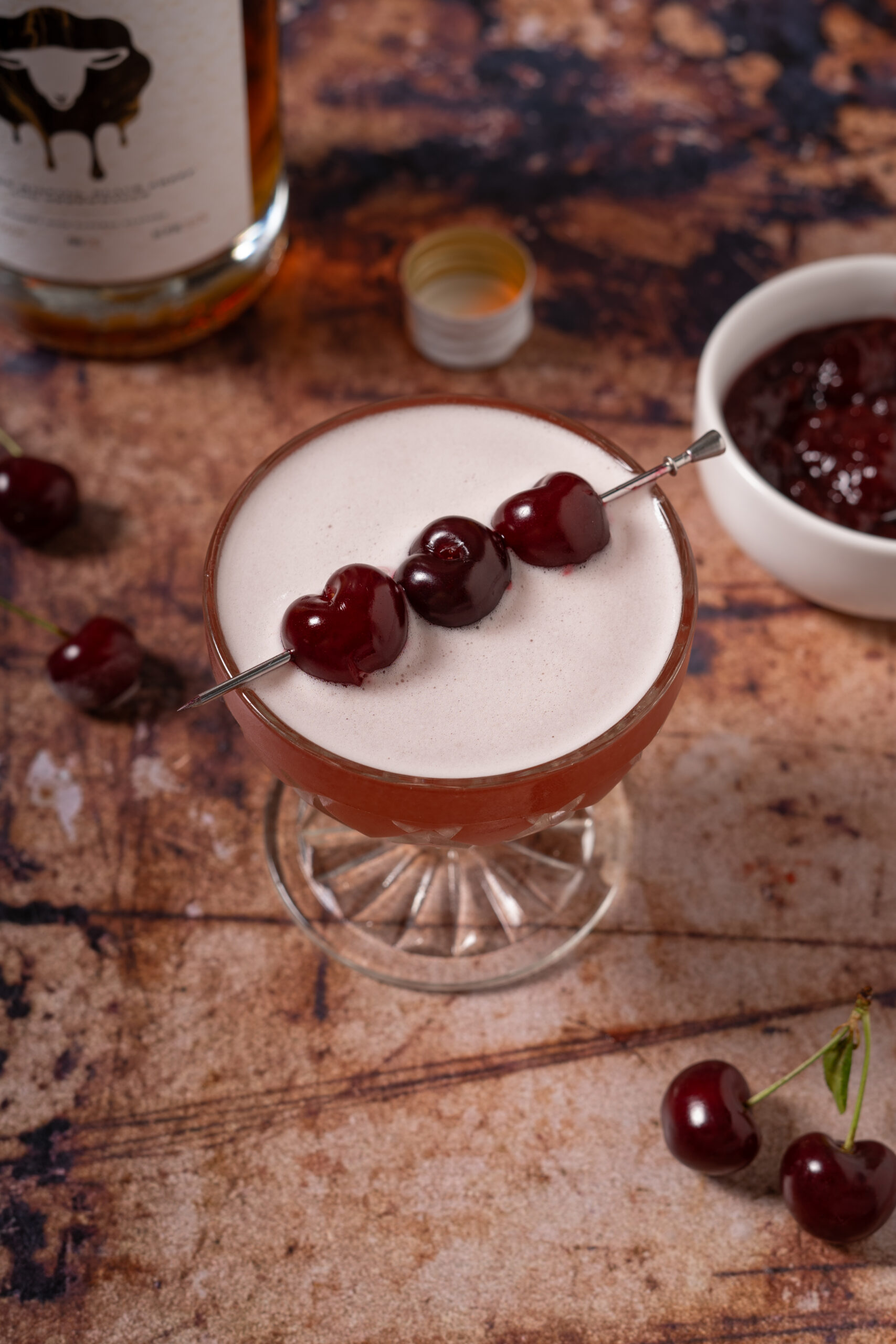 whiskey sour with cherry garnish in coupe glass.