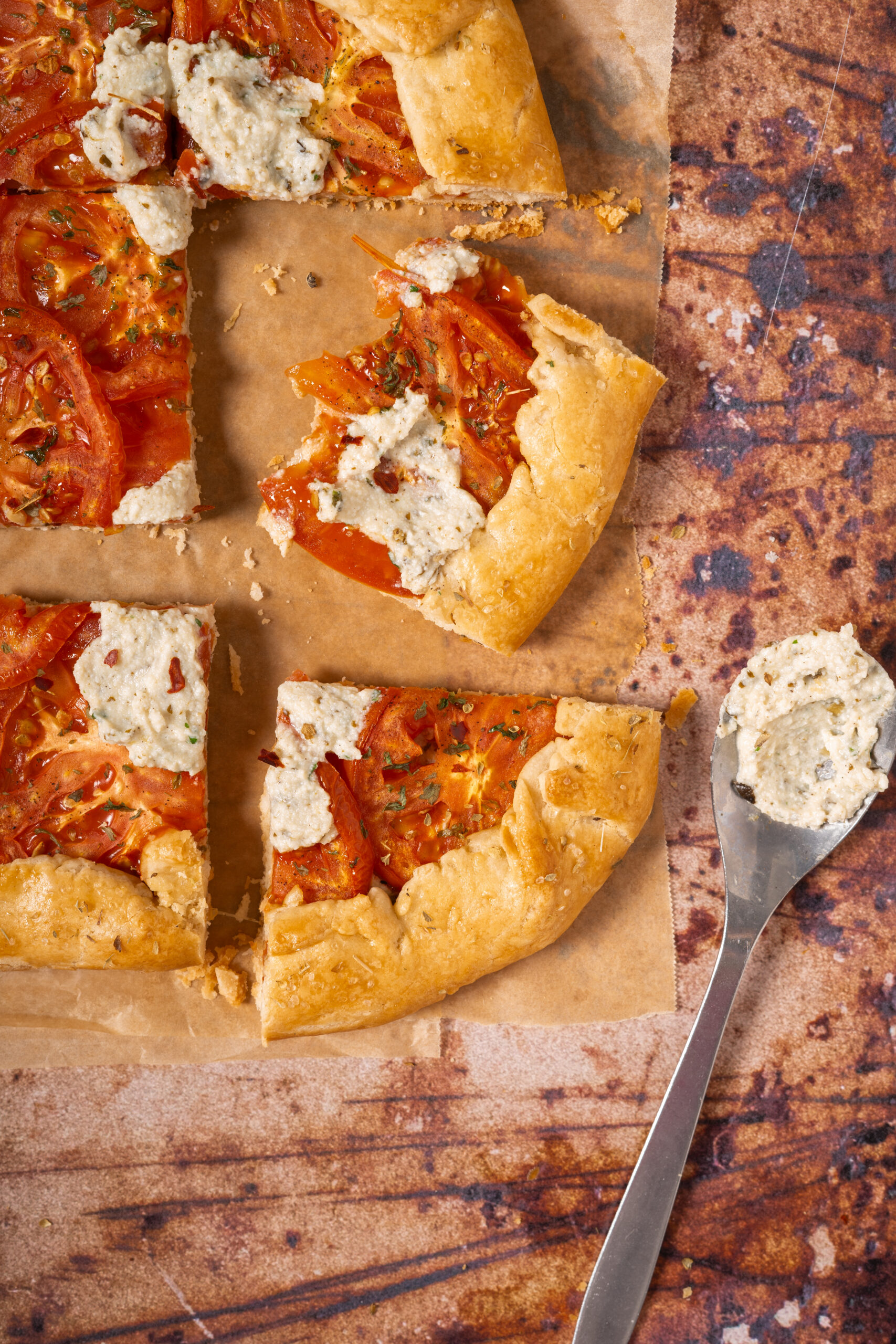 sliced tomato ricotta galette on parchment paper with spoon.