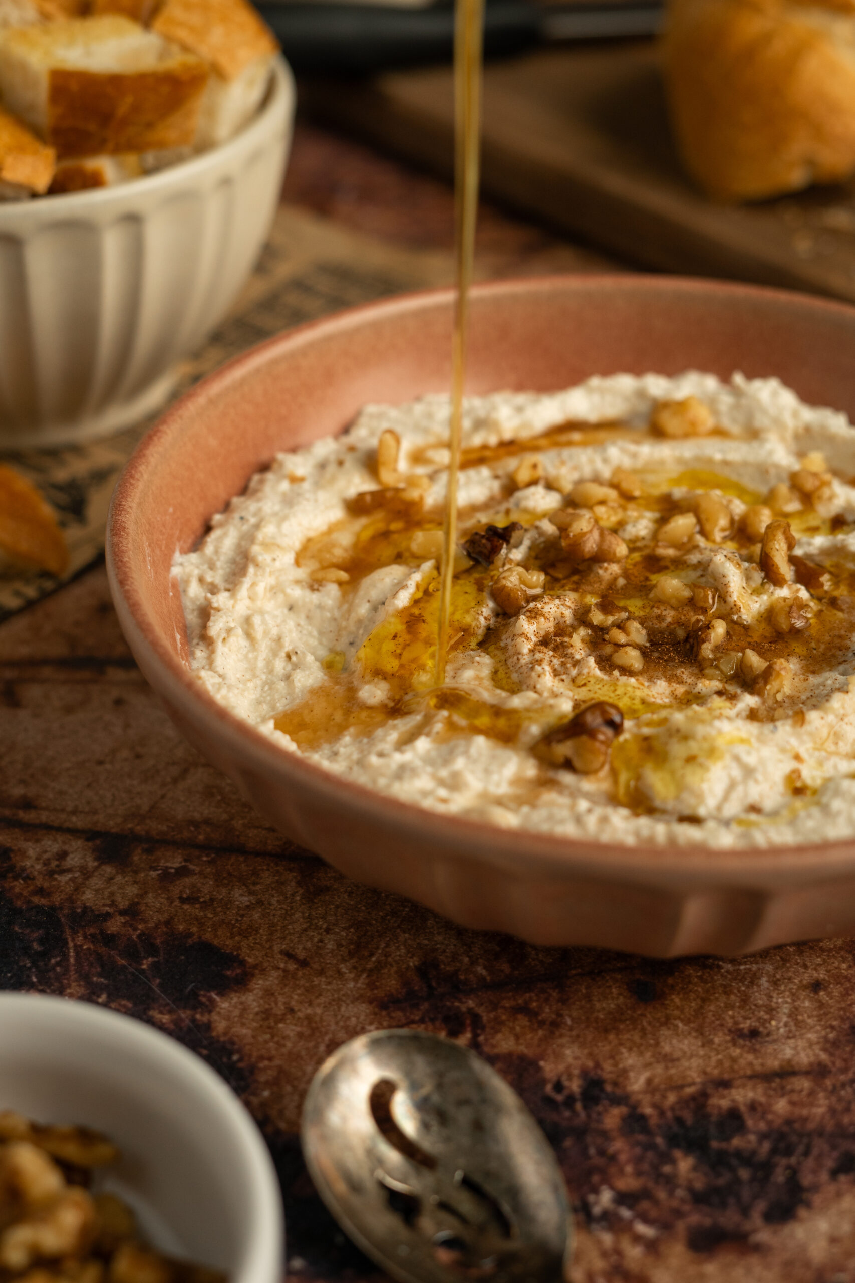 olive oil drizzled into whipped feta dip in pink bowl with syrup and walnuts.