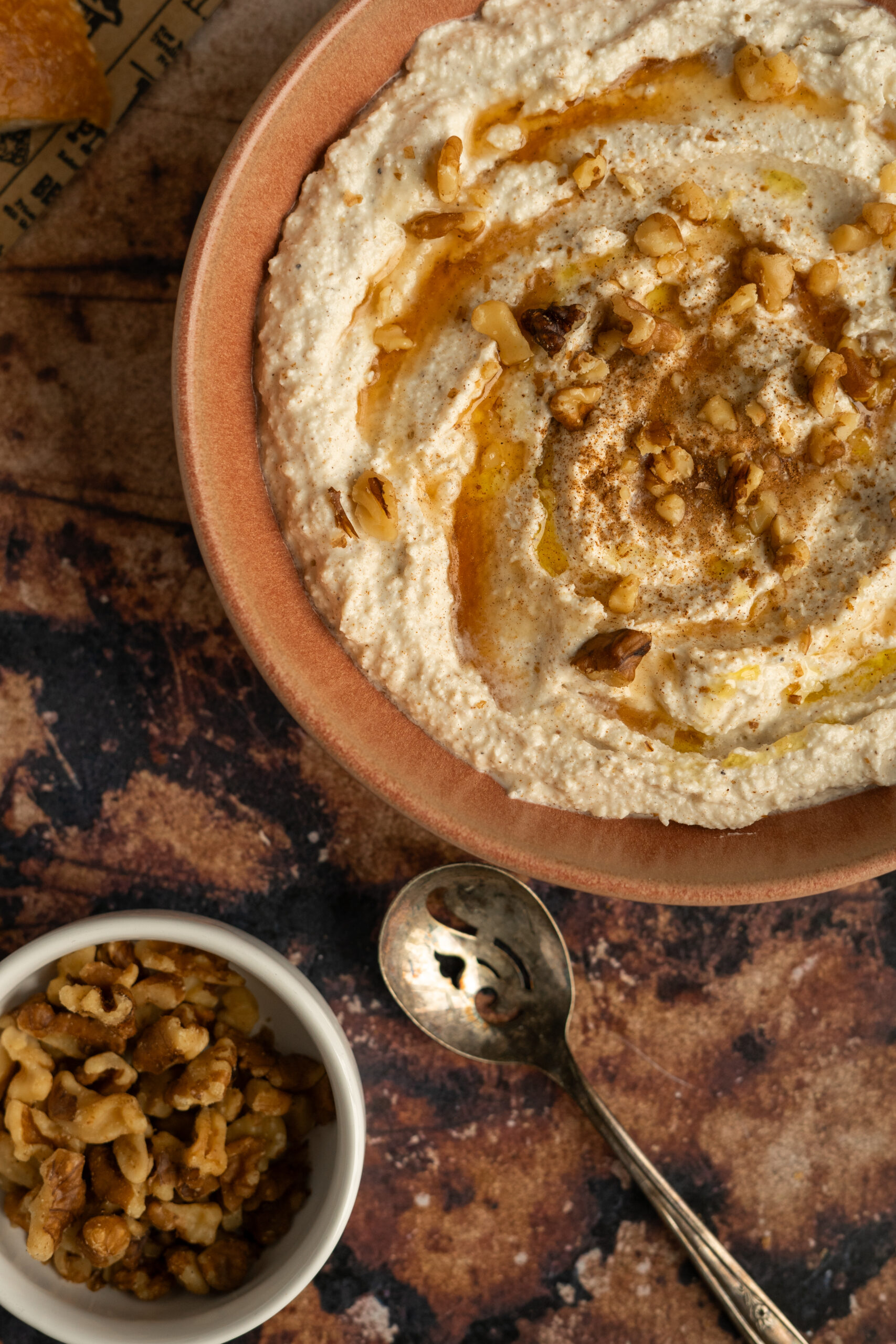 close up of whipped feta dip in pink bowl with syrup and walnuts.