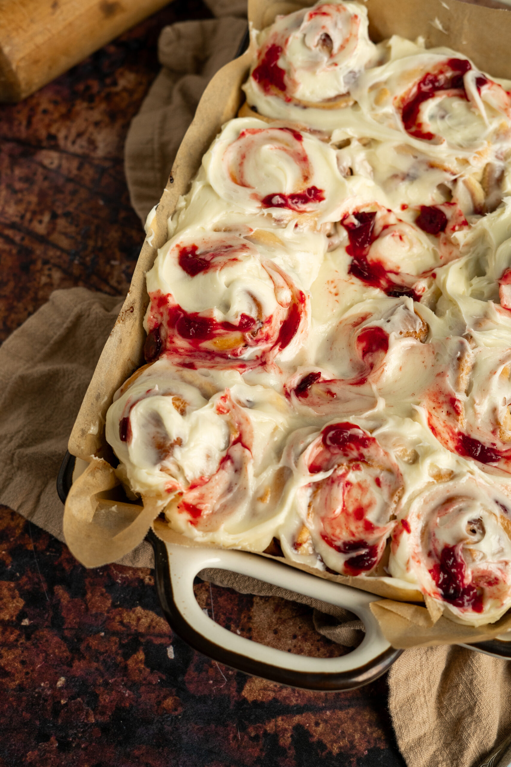 plum cinnamon rolls with cream cheese frosting and plum jam in baking dish.