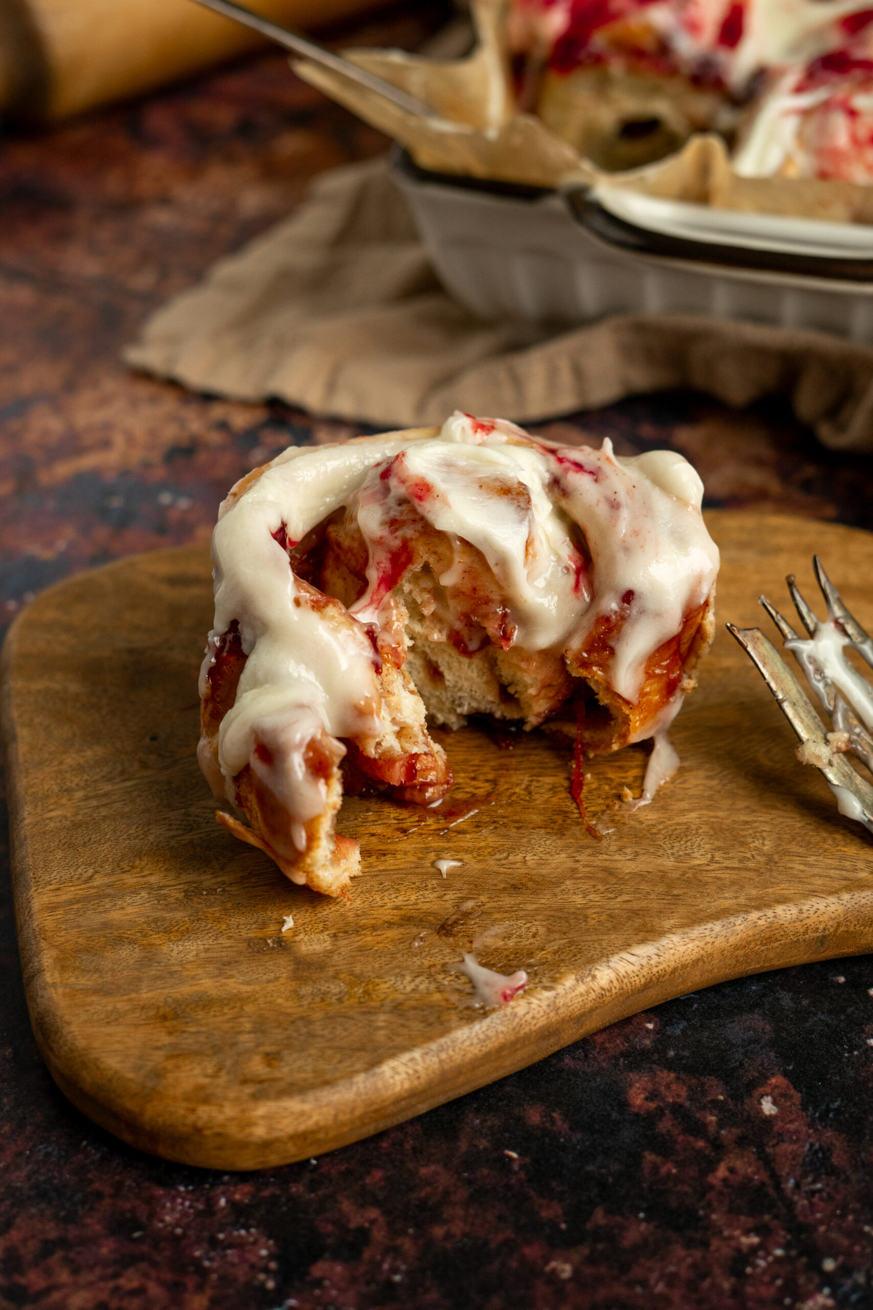 plum cinnamon roll on wooden board with bite taken out.