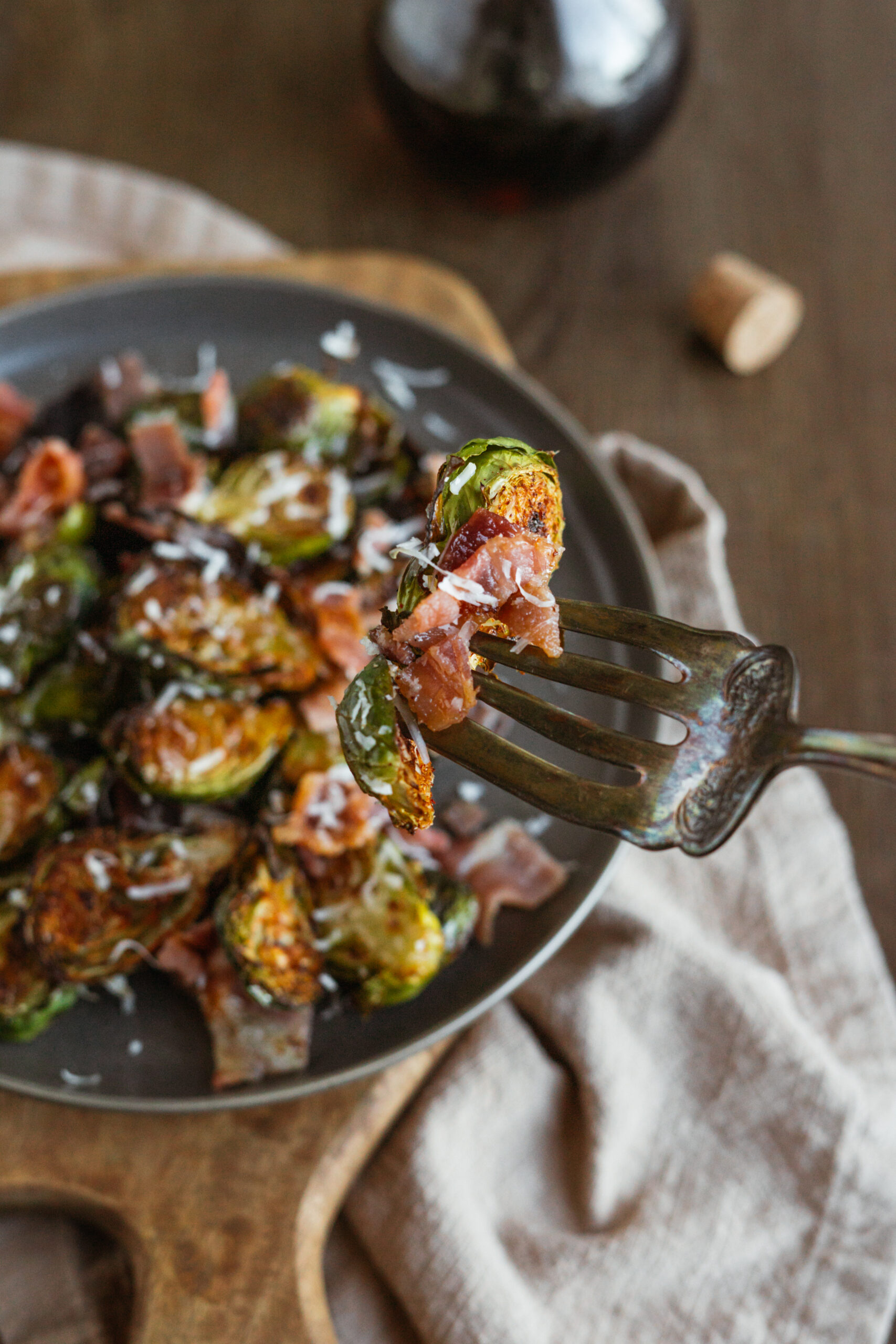 fork holding up maple bacon brussels sprout over a dark plate with vintage fork.