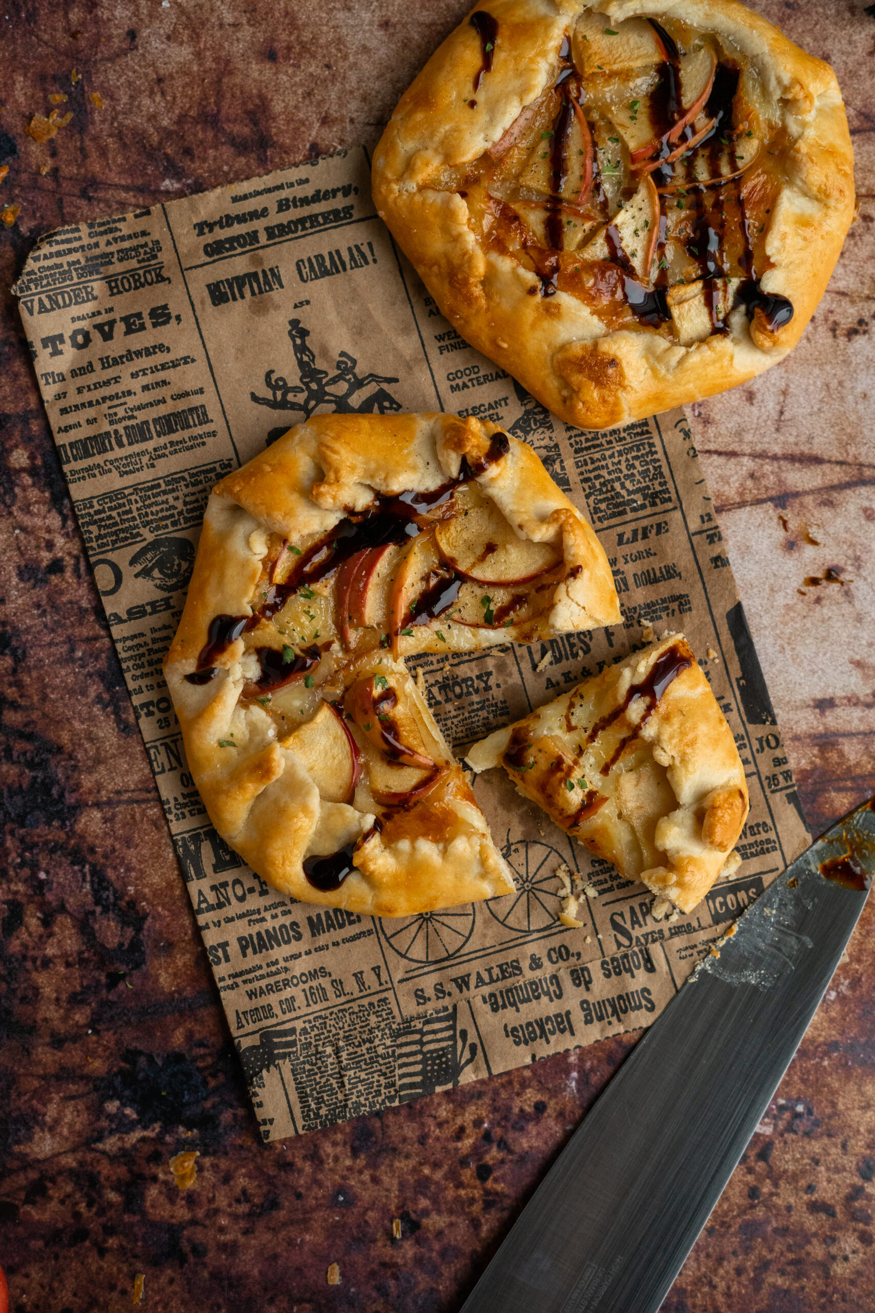 close up of mini brie and apple galettes on newspaper with a slice taken out.