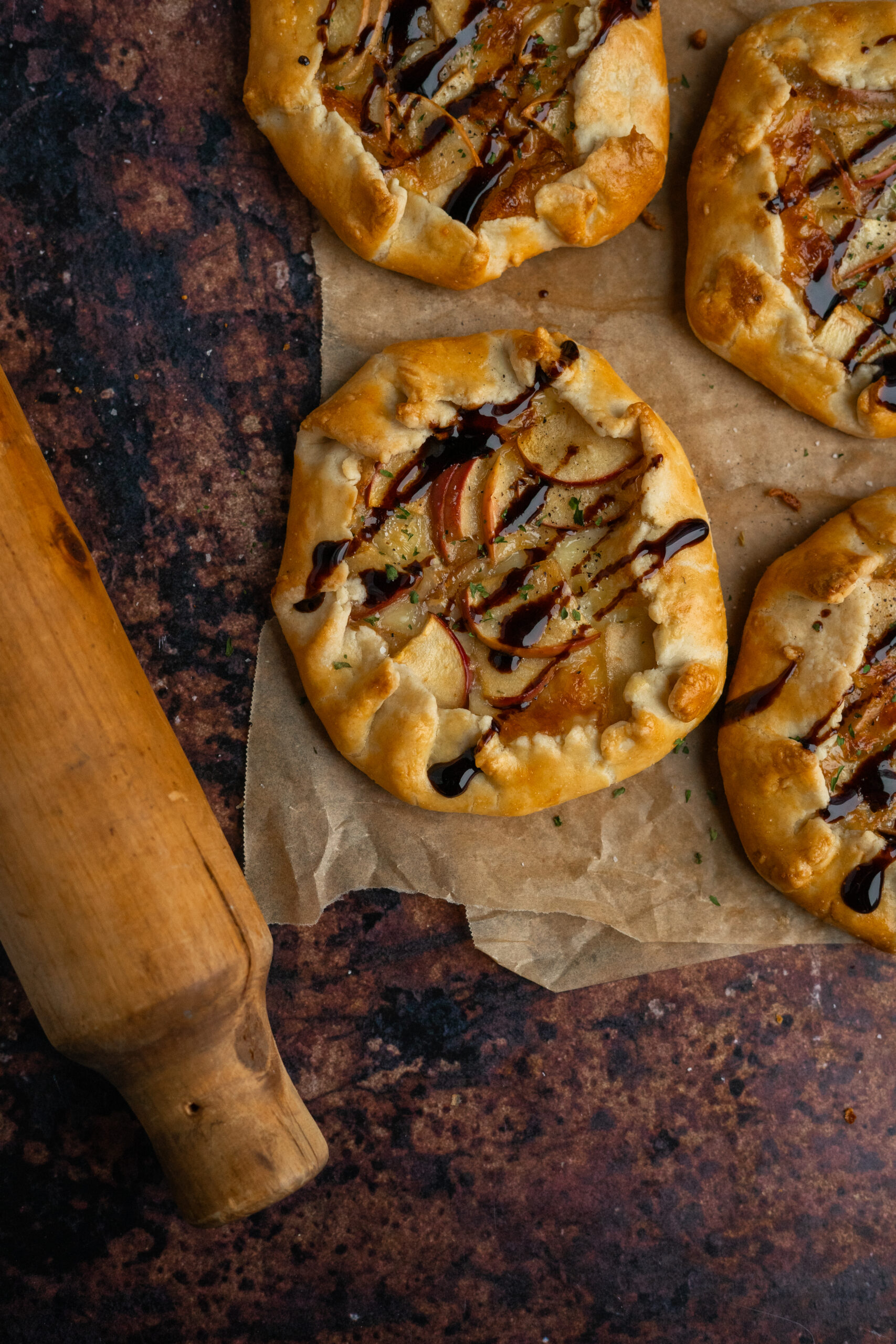 close up of mini brie and apple galettes on parchment paper with wooden rolling pin.