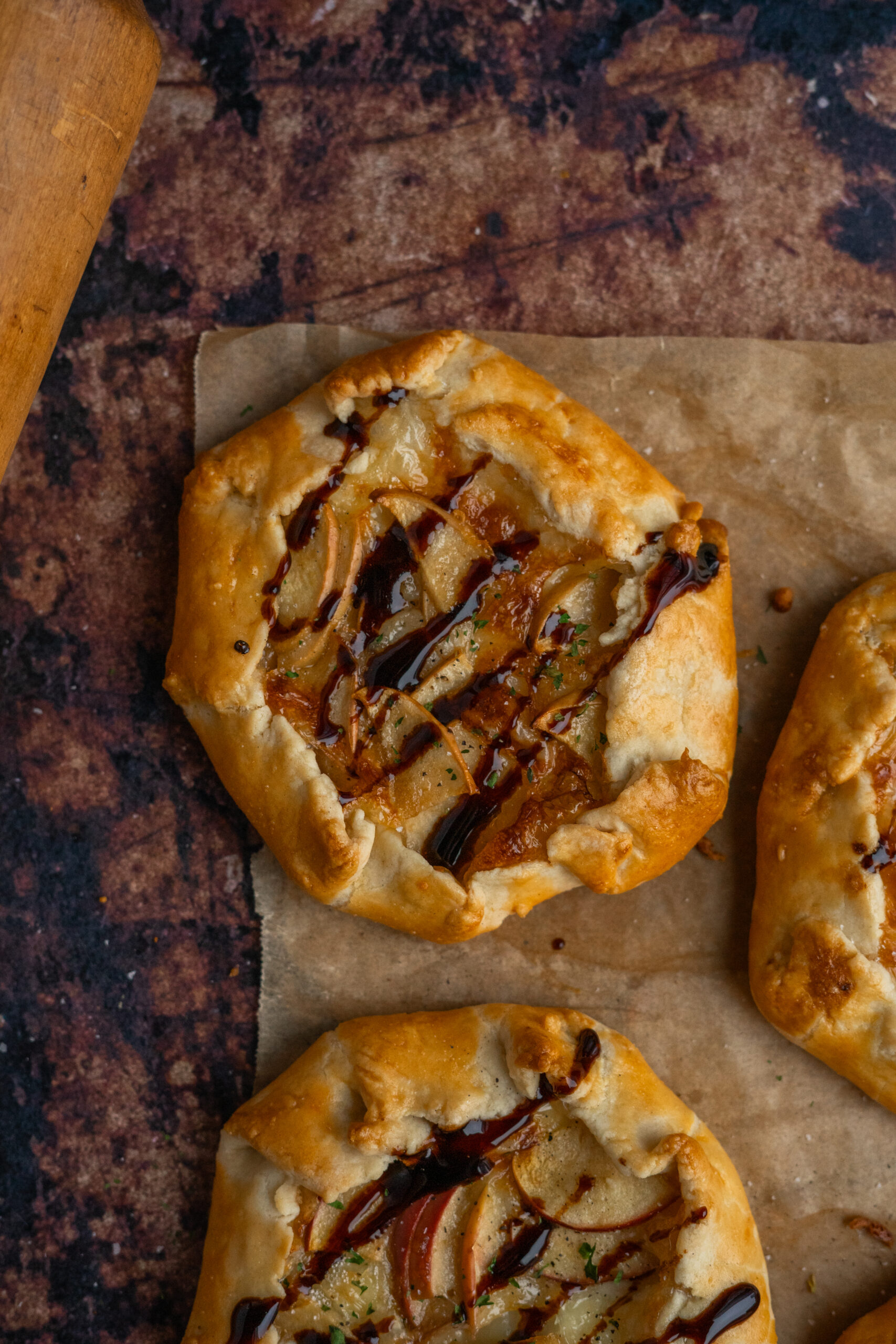 close up of mini brie and apple galette on parchment paper with wooden rolling pin in corner.