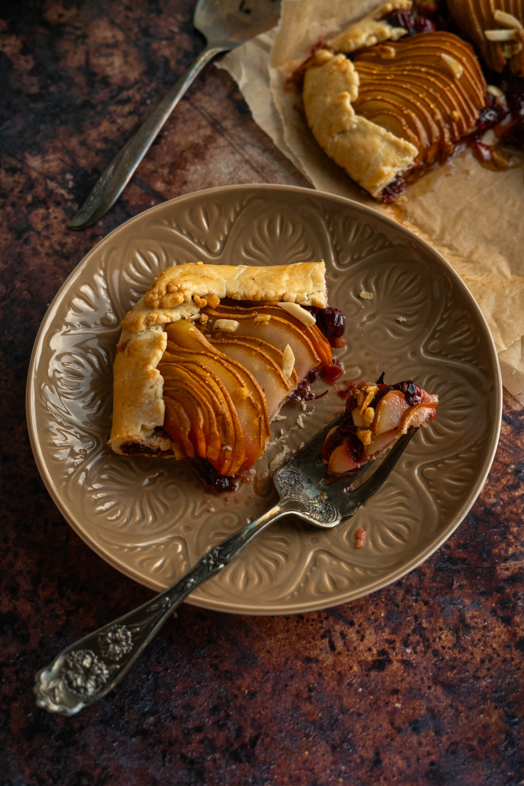 close up of sliced cranberry pear galette on brown plate with vintage fork.