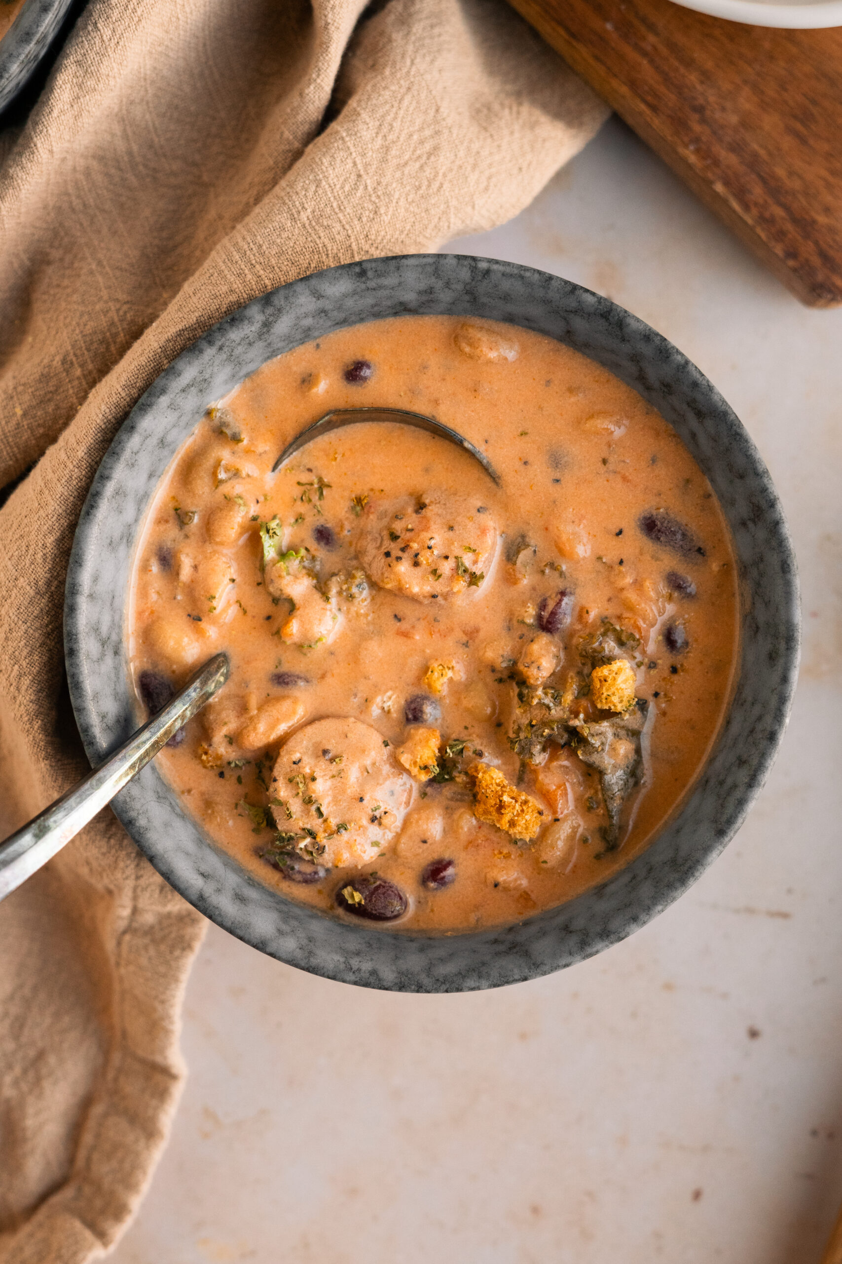 bean and sausage soup in a blue bowl on a beige background.