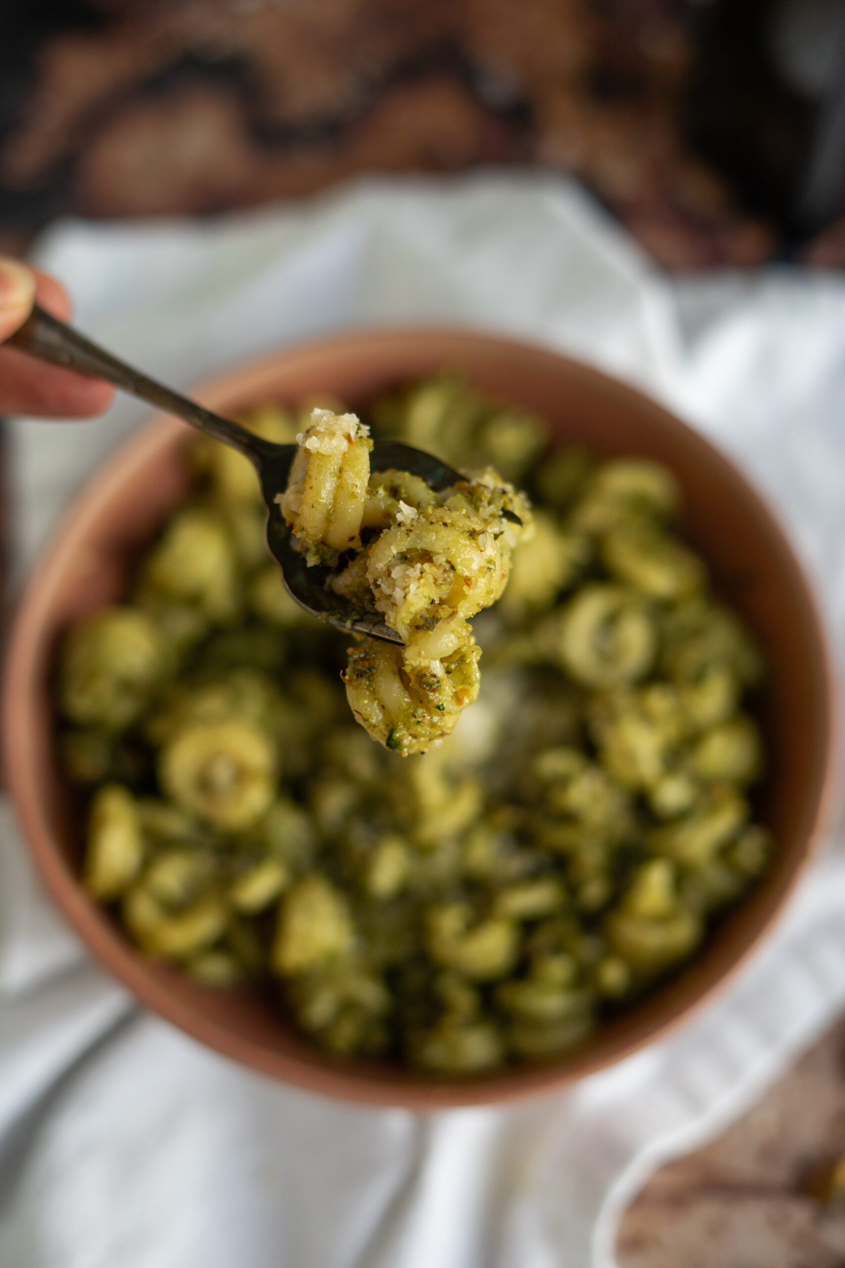 close up of forkful of pistachio pesto pasta with bowl in the background.