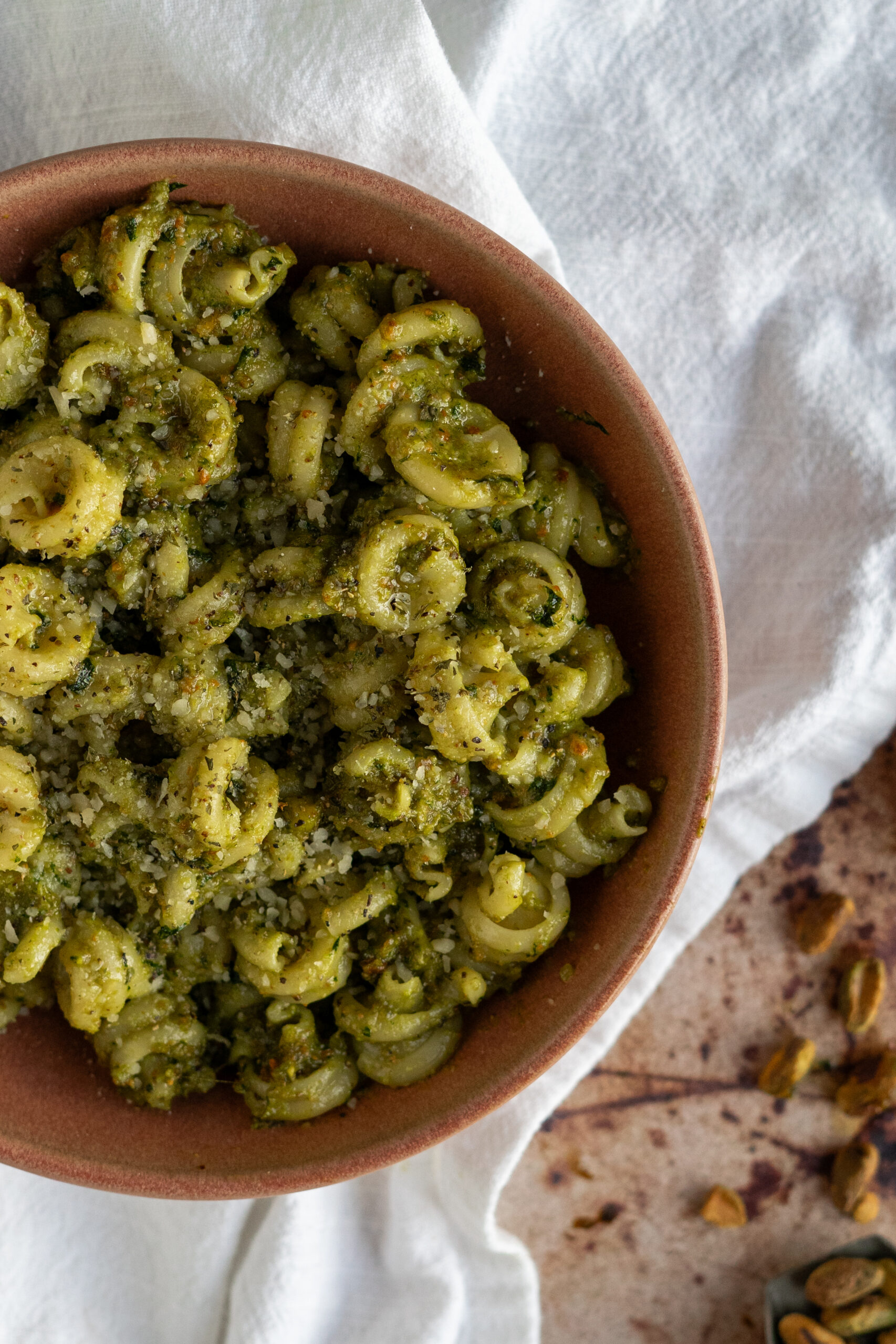 close up of pistachio pesto pasta in pink bowl on white napkin.