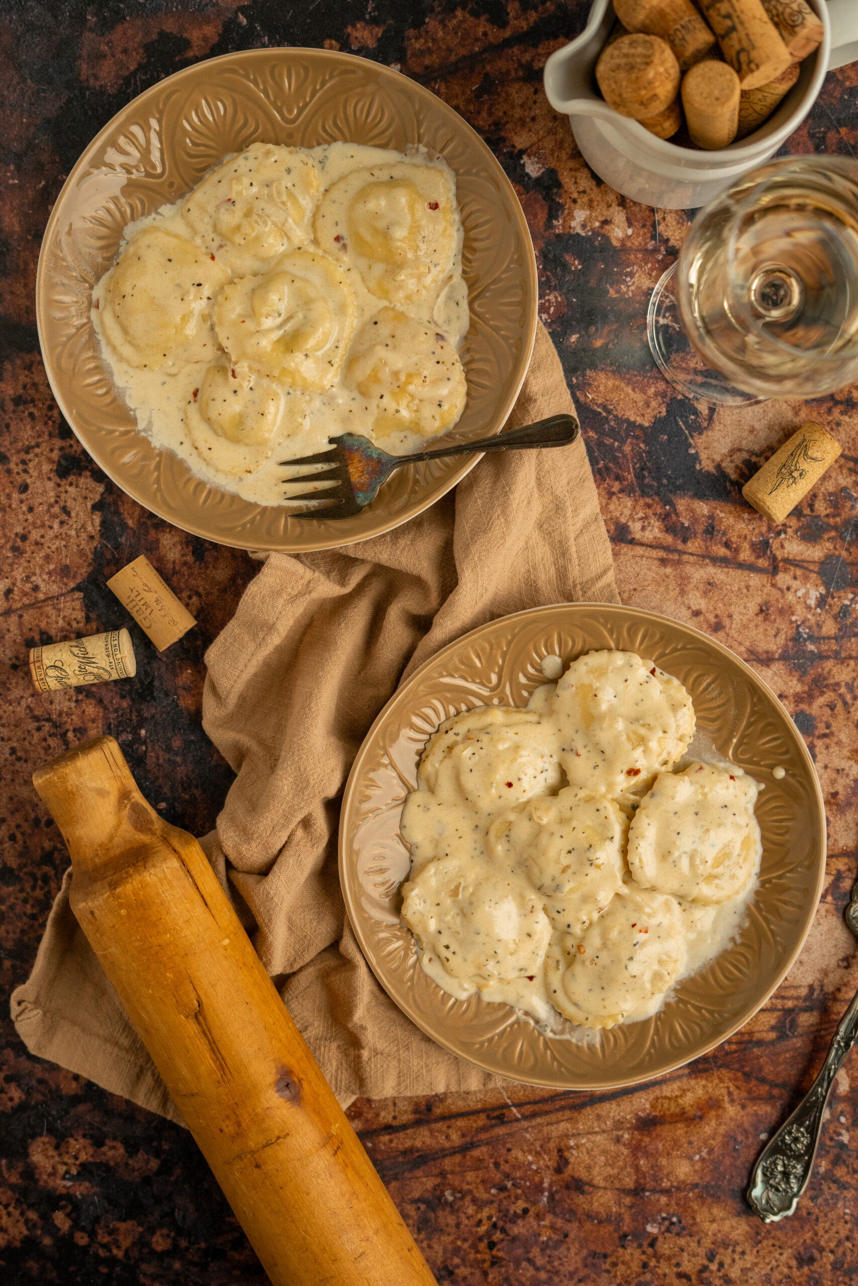 two plates of ravioli in white wine sauce on brown surface.