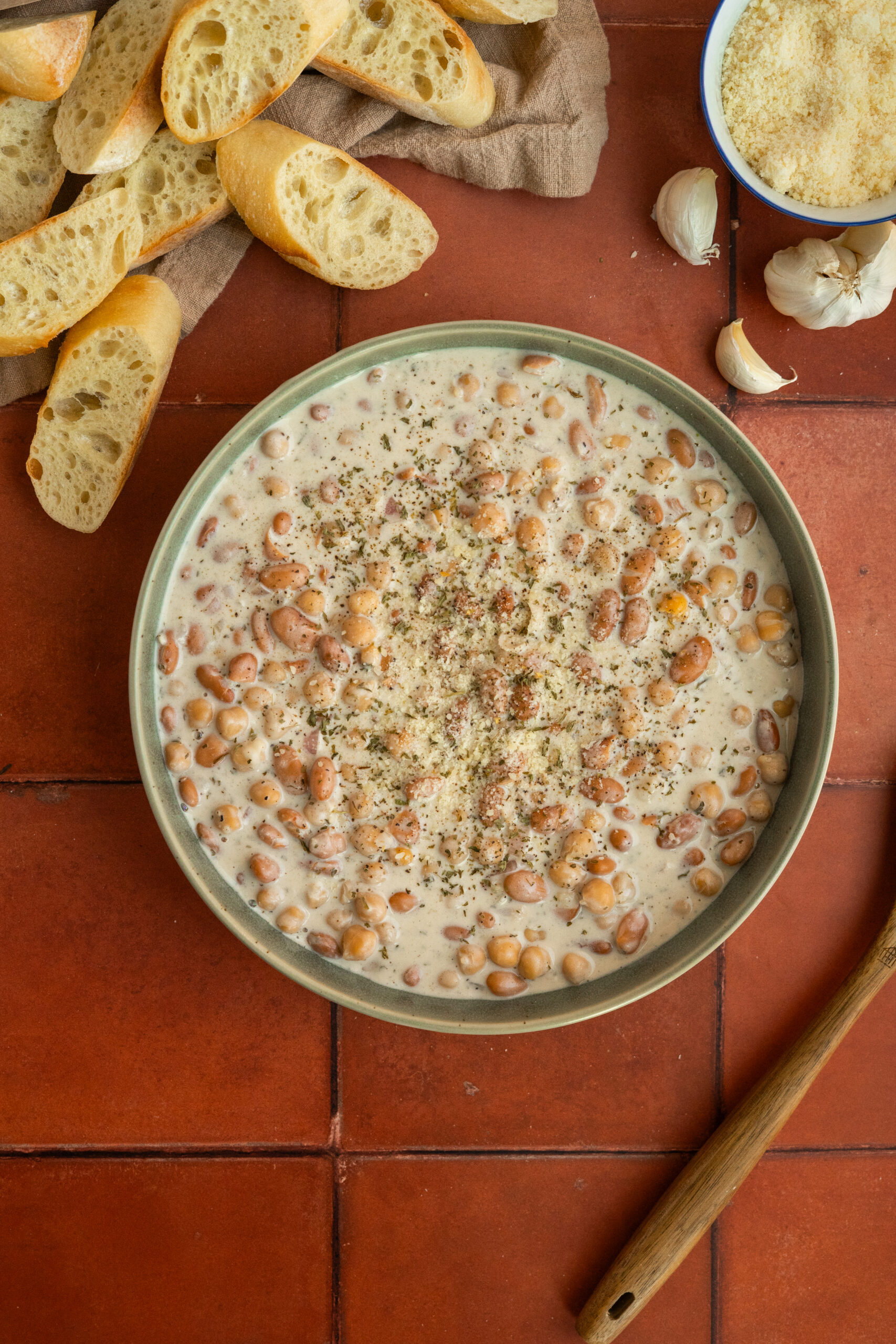 creamy beans and chickpeas in green bowl on red tile background.