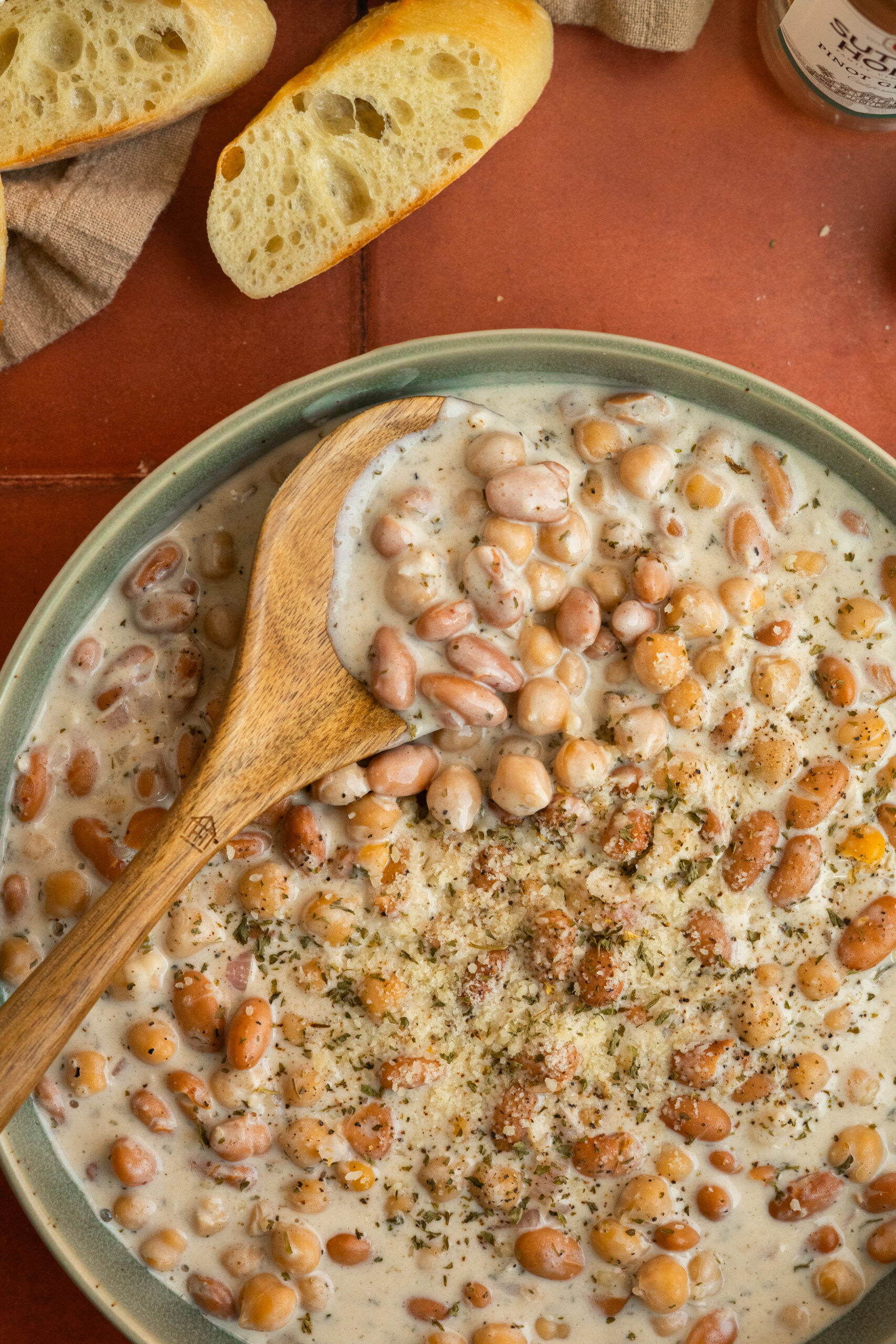 close up creamy beans and chickpeas in green bowl with wooden spoon in bowl.