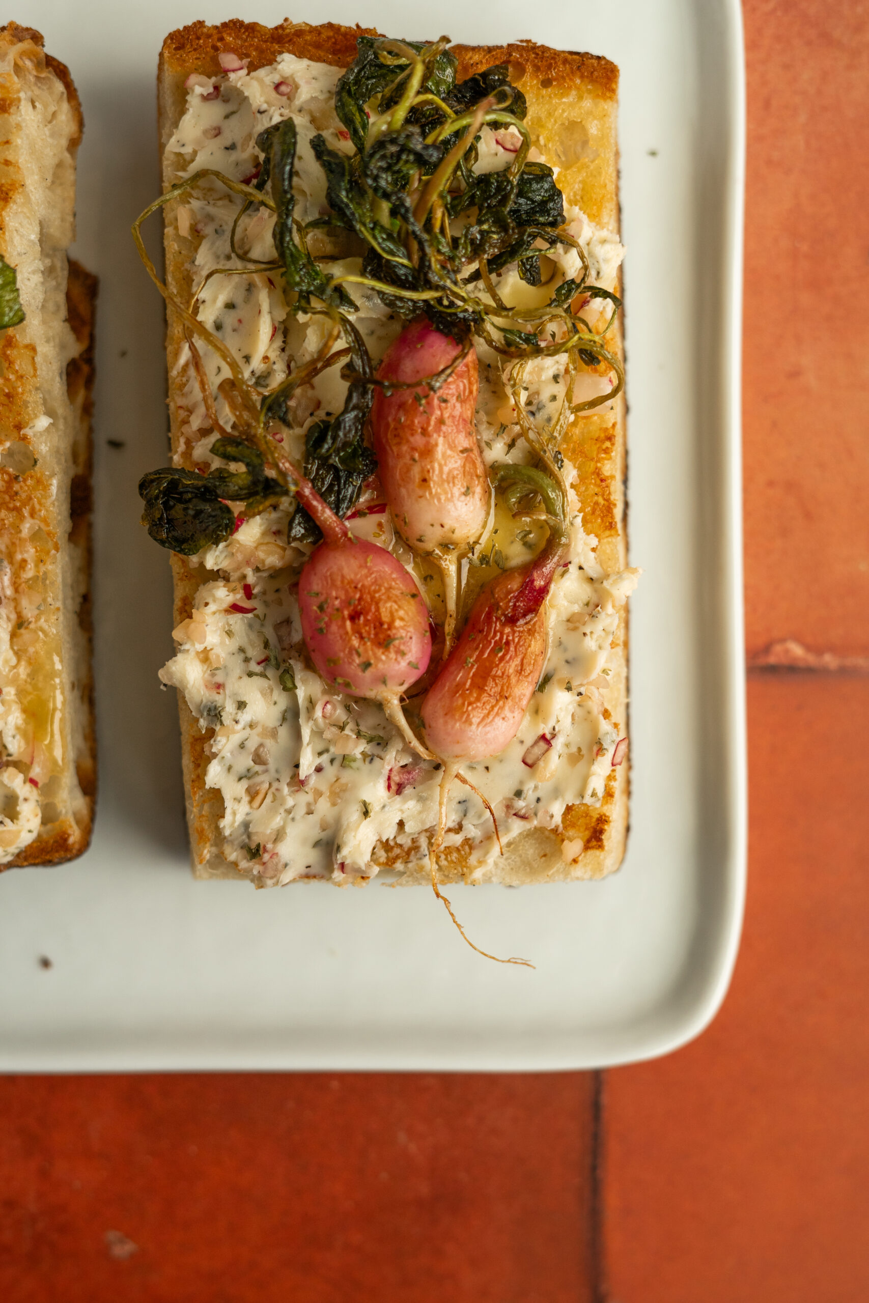 close up of toasted focaccia with radish butter and roasted radishes on top.