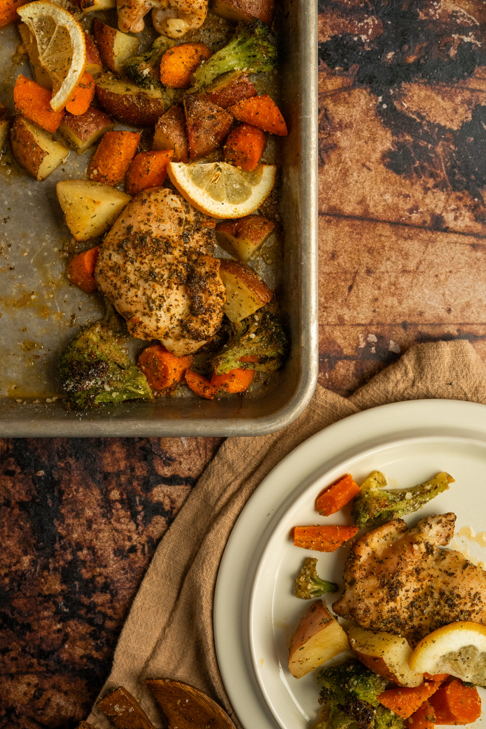 corner of sheet pan of chicken thighs and roasted vegetables with plate to the side.