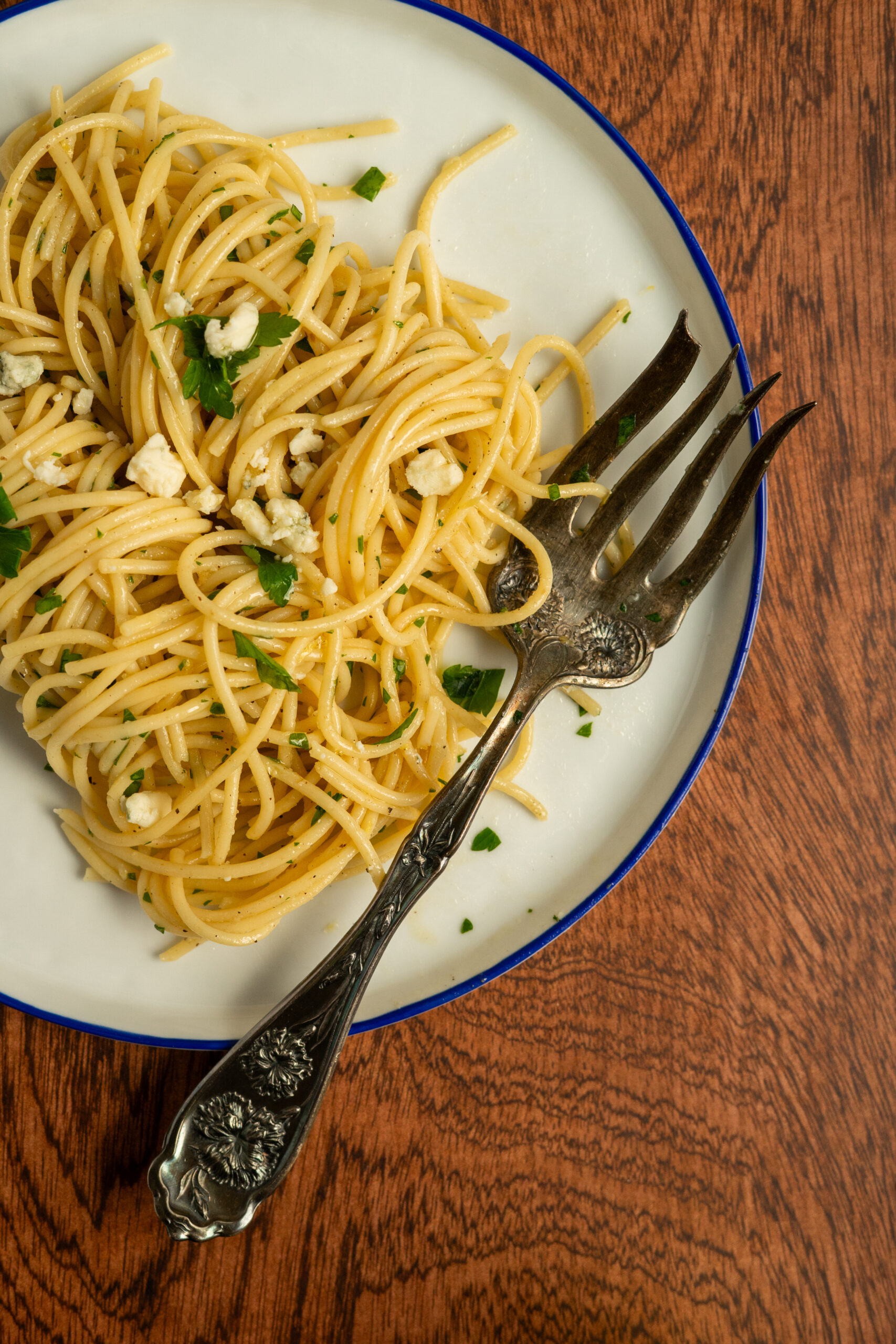 dirty martini pasta on white plate with vintage fork on wooden surface.