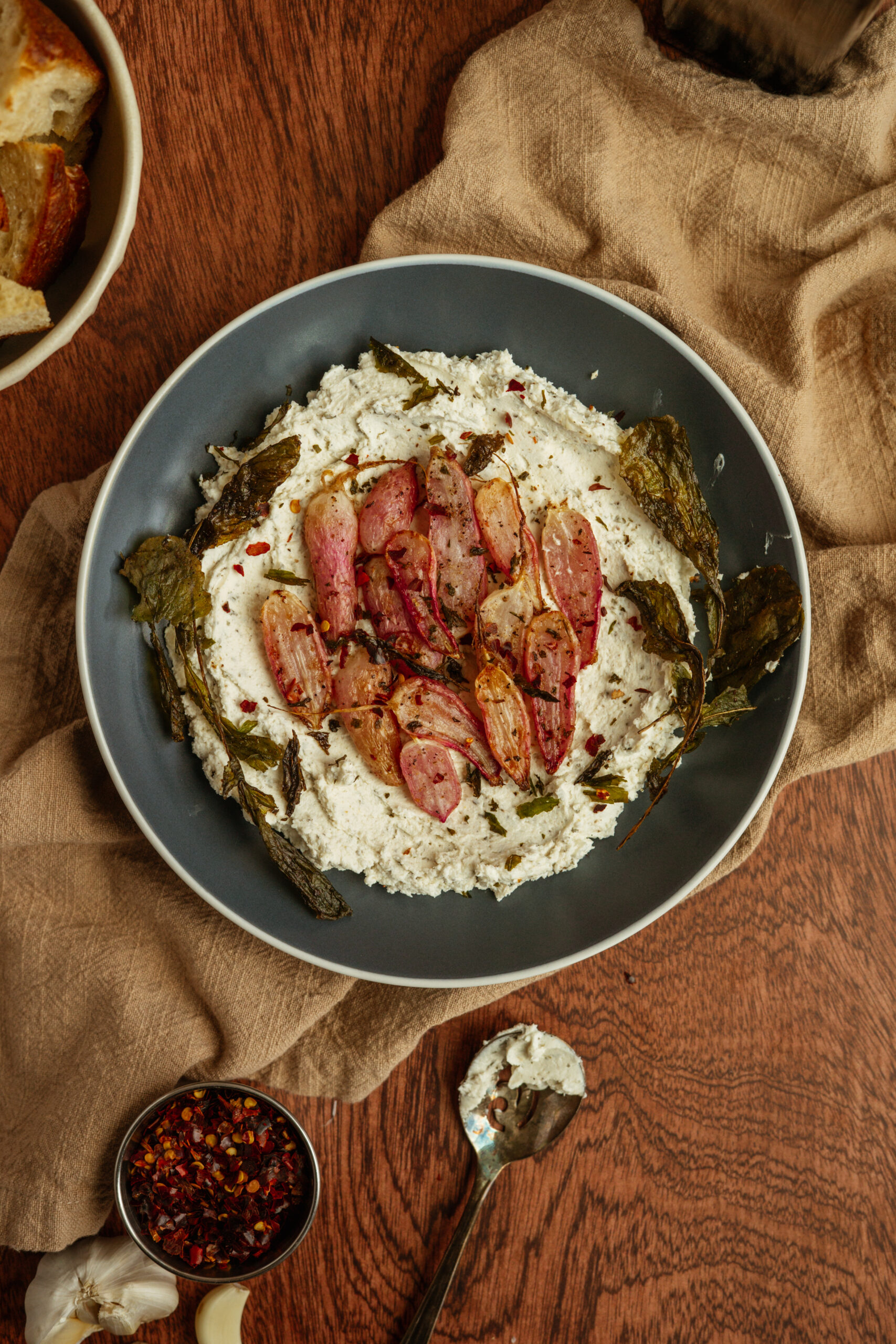 overhead of goat cheese with roasted radishes in blue bowl on wooden surface.