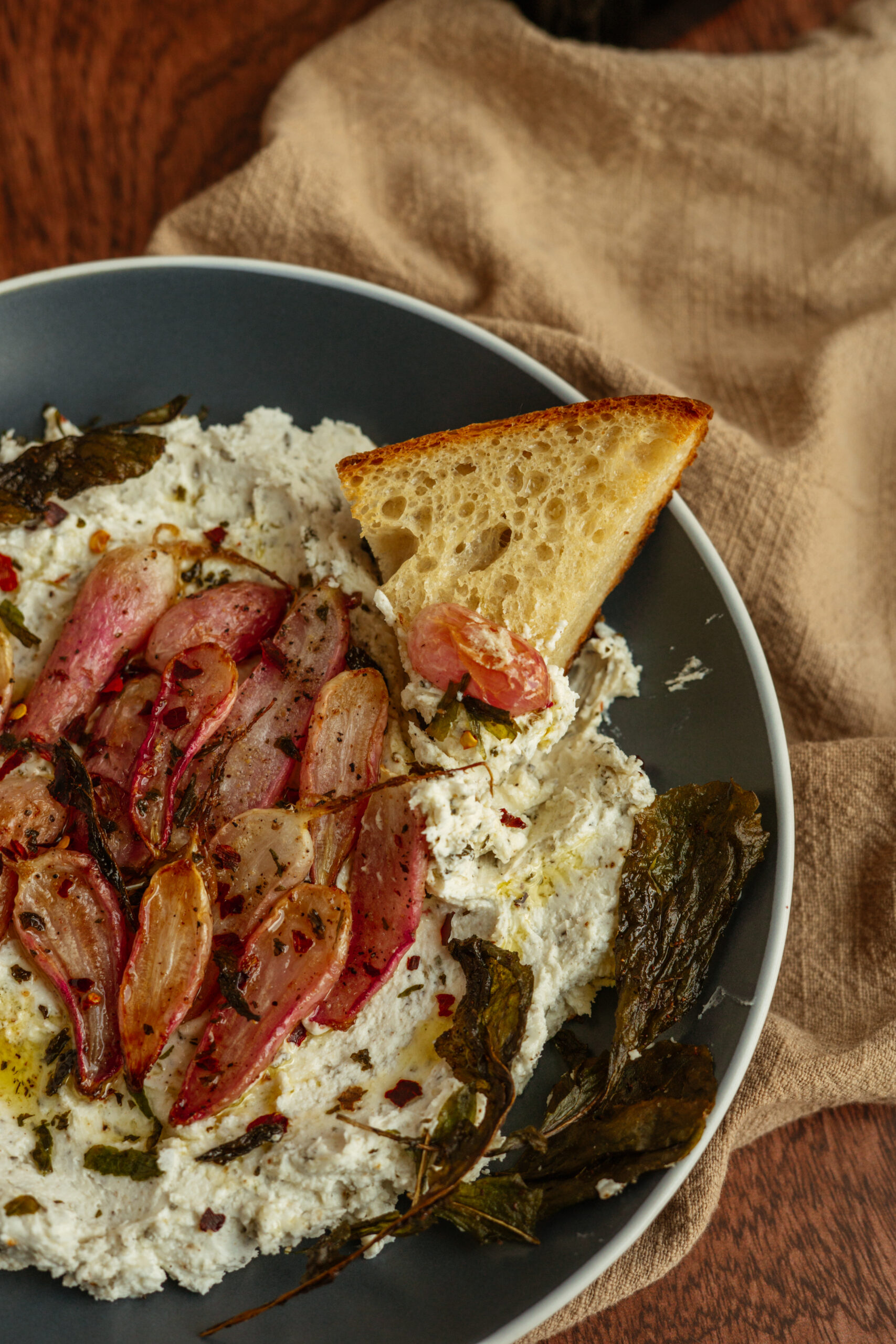 toasted bread on top of goat cheese with roasted radishes in blue bowl.