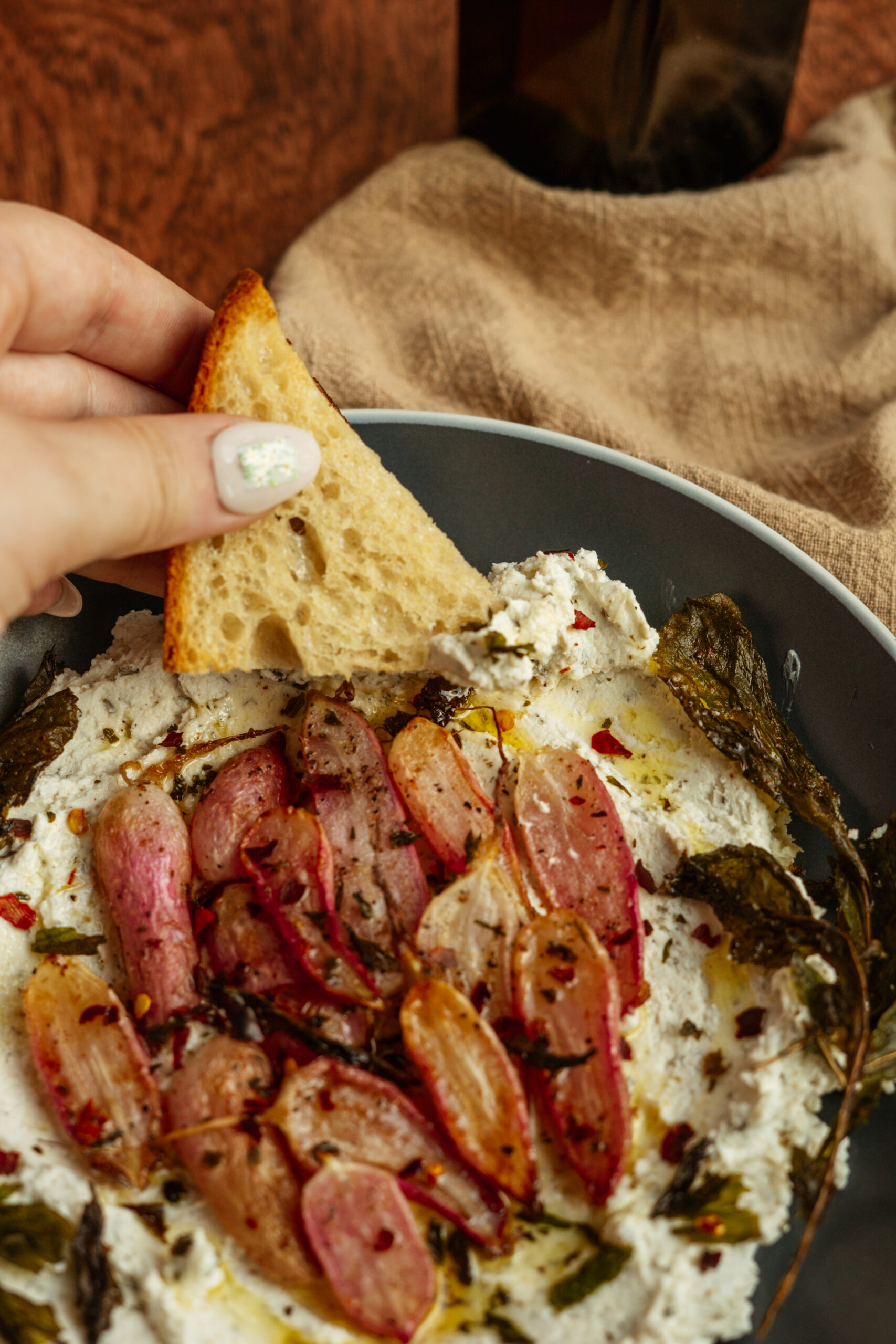 toasted bread being dipped into goat cheese with roasted radishes.