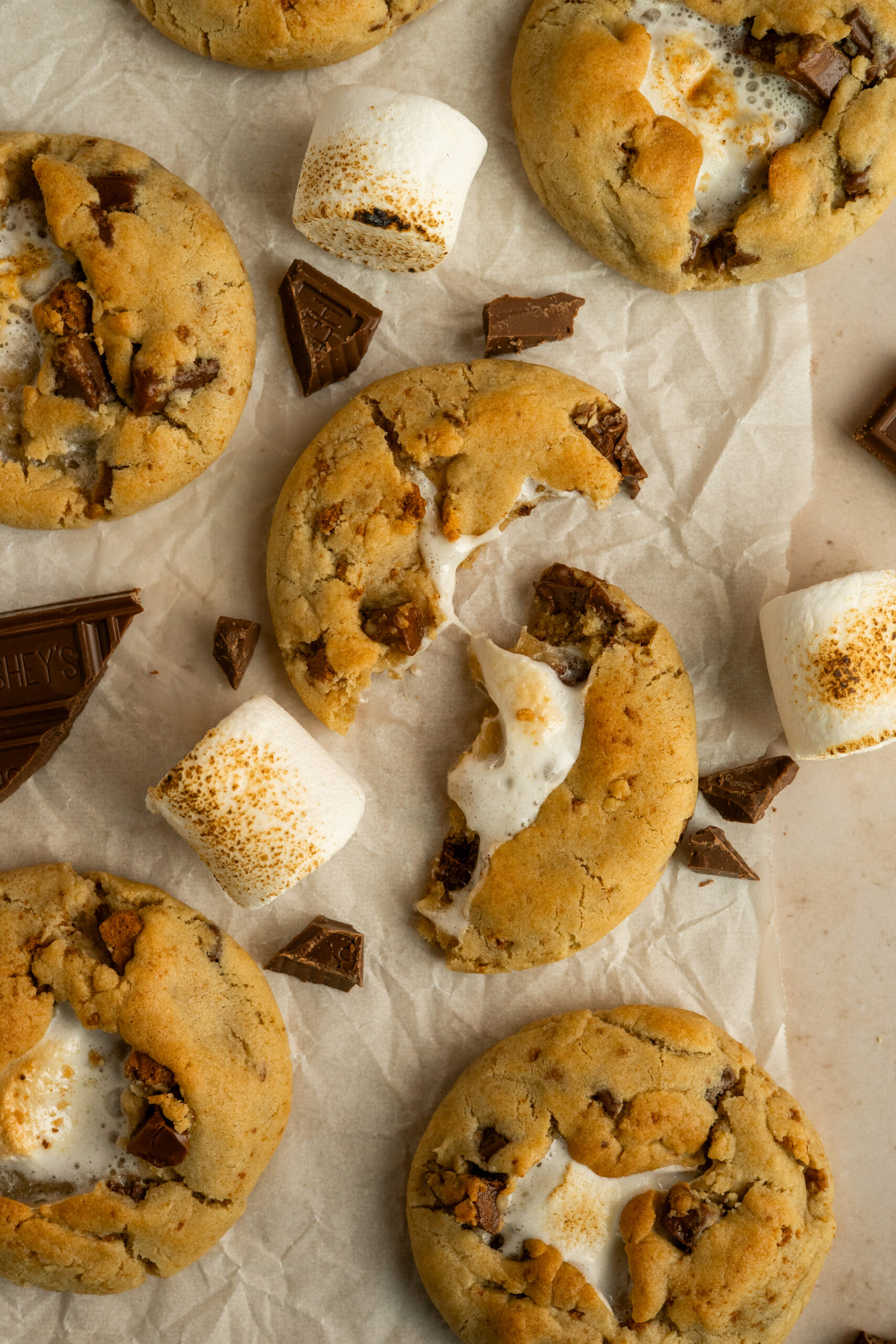 s'mores cookie broken in half surrounded by chocolate and marshmallows.