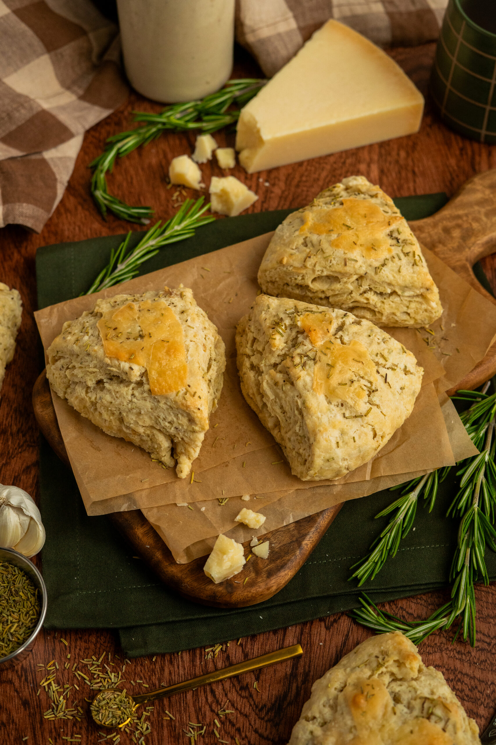parmesan garlic scones on wooden board with rosemary sprigs and parmesan wedge in background.