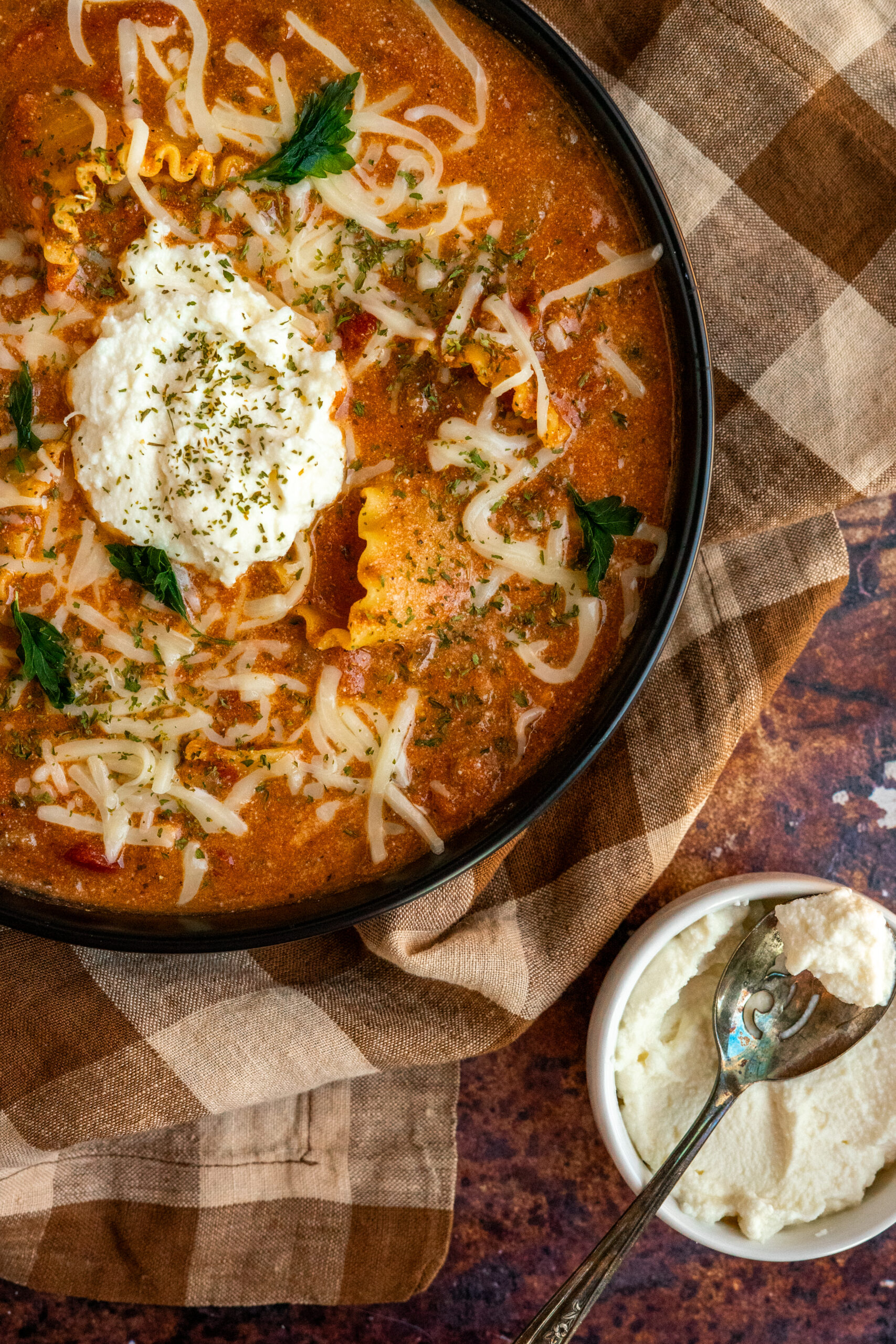 overhead close up of lasagna soup with a small bowl of ricotta to the side.