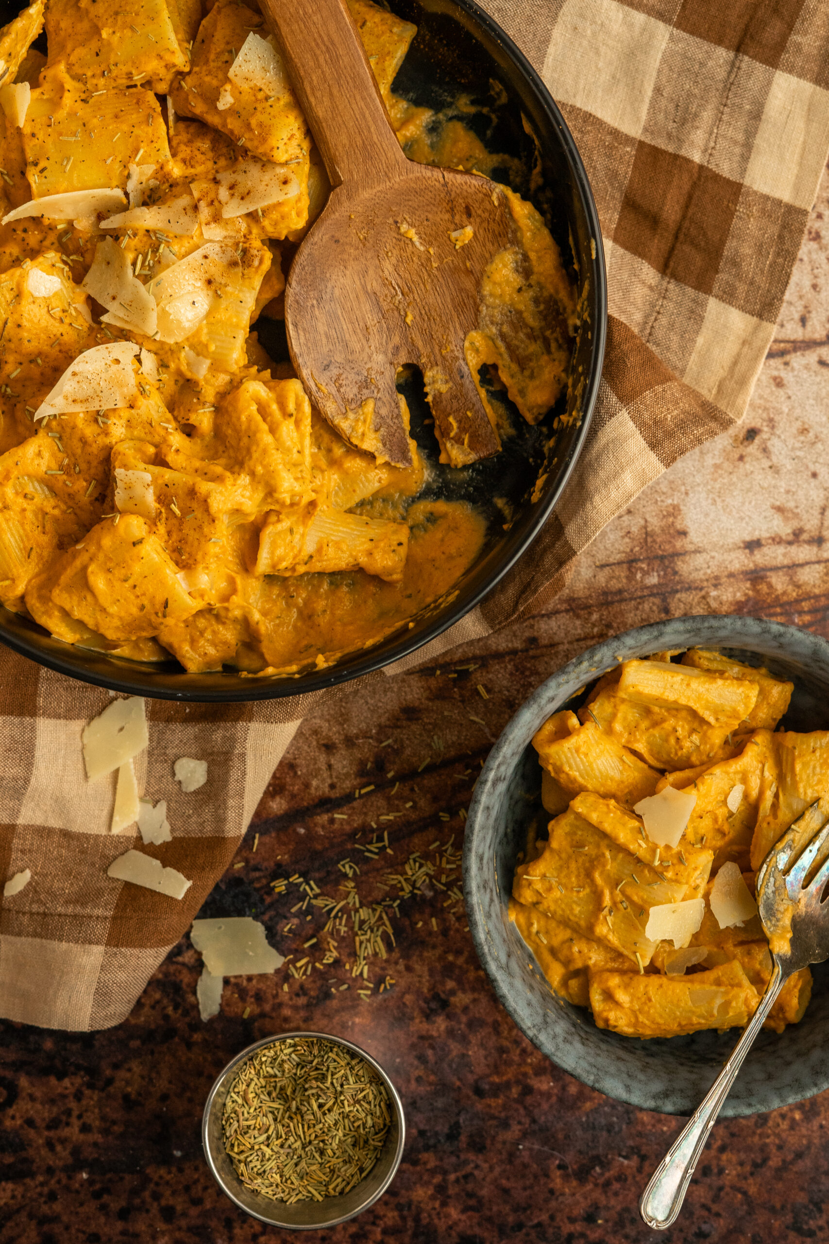 pumpkin pasta in black bowl with wooden spoon and a smaller bowl of pasta below.