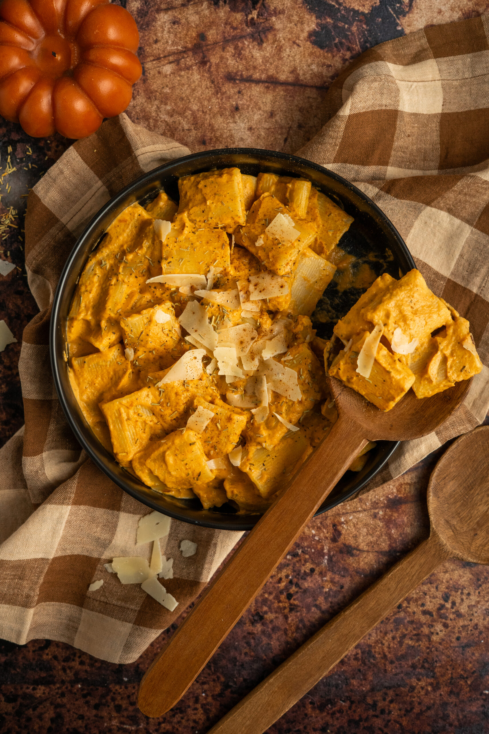 pumpkin pasta in black bowl with wooden spoon resting on bowl.