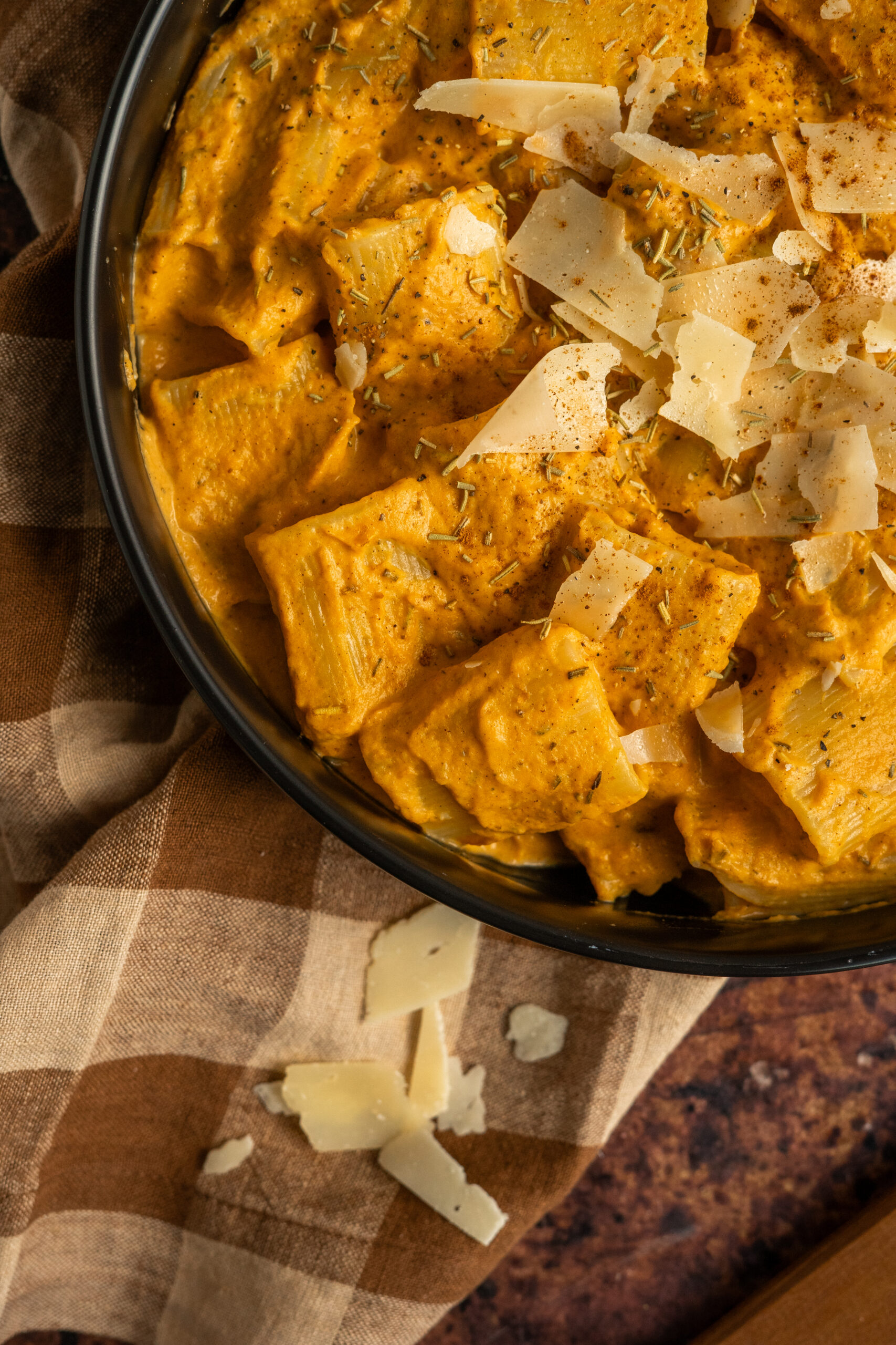 close up of pumpkin pasta in black bowl on a gingham napkin.