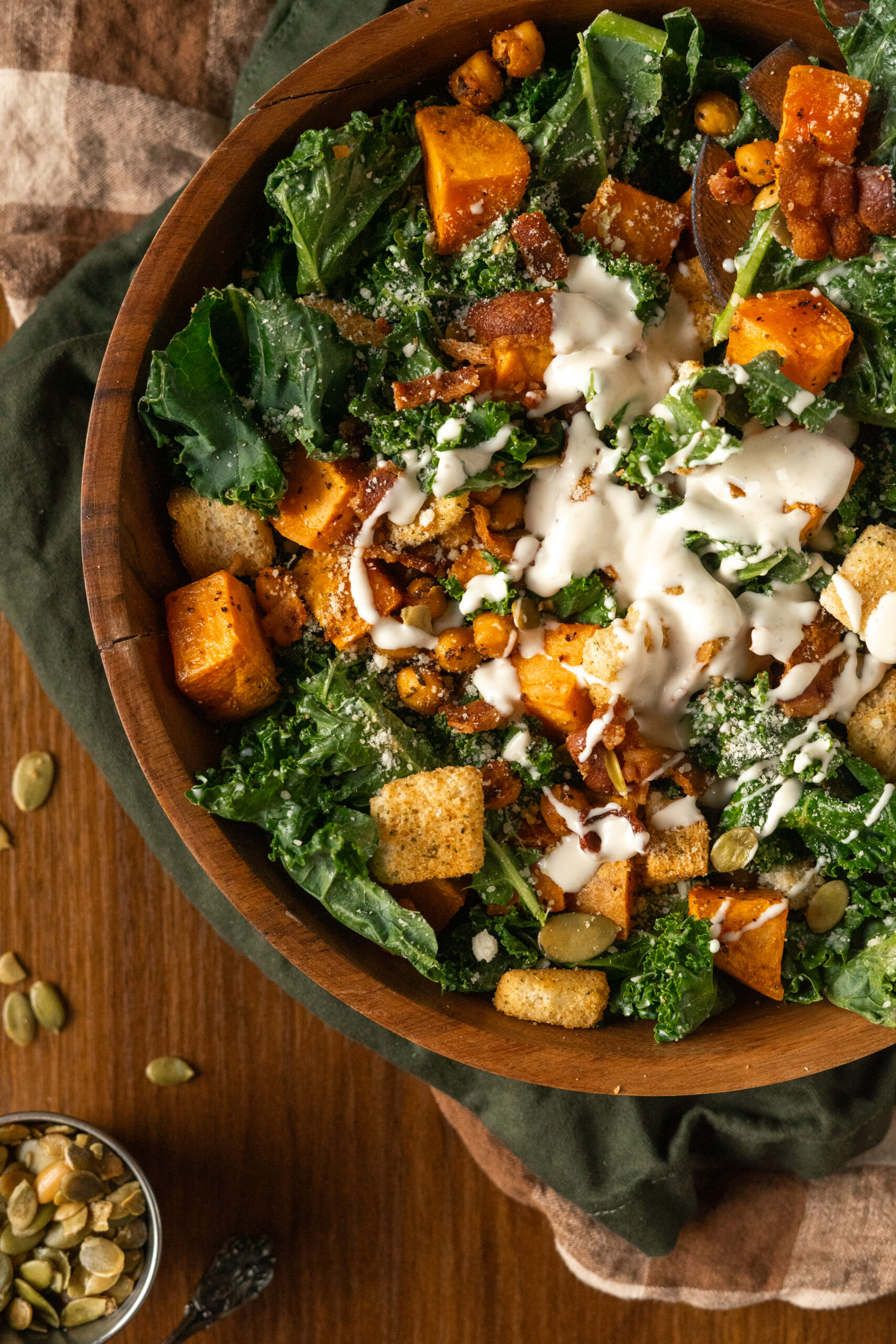 close up of kale caesar salad in wooden bowl with dressing poured on salad.