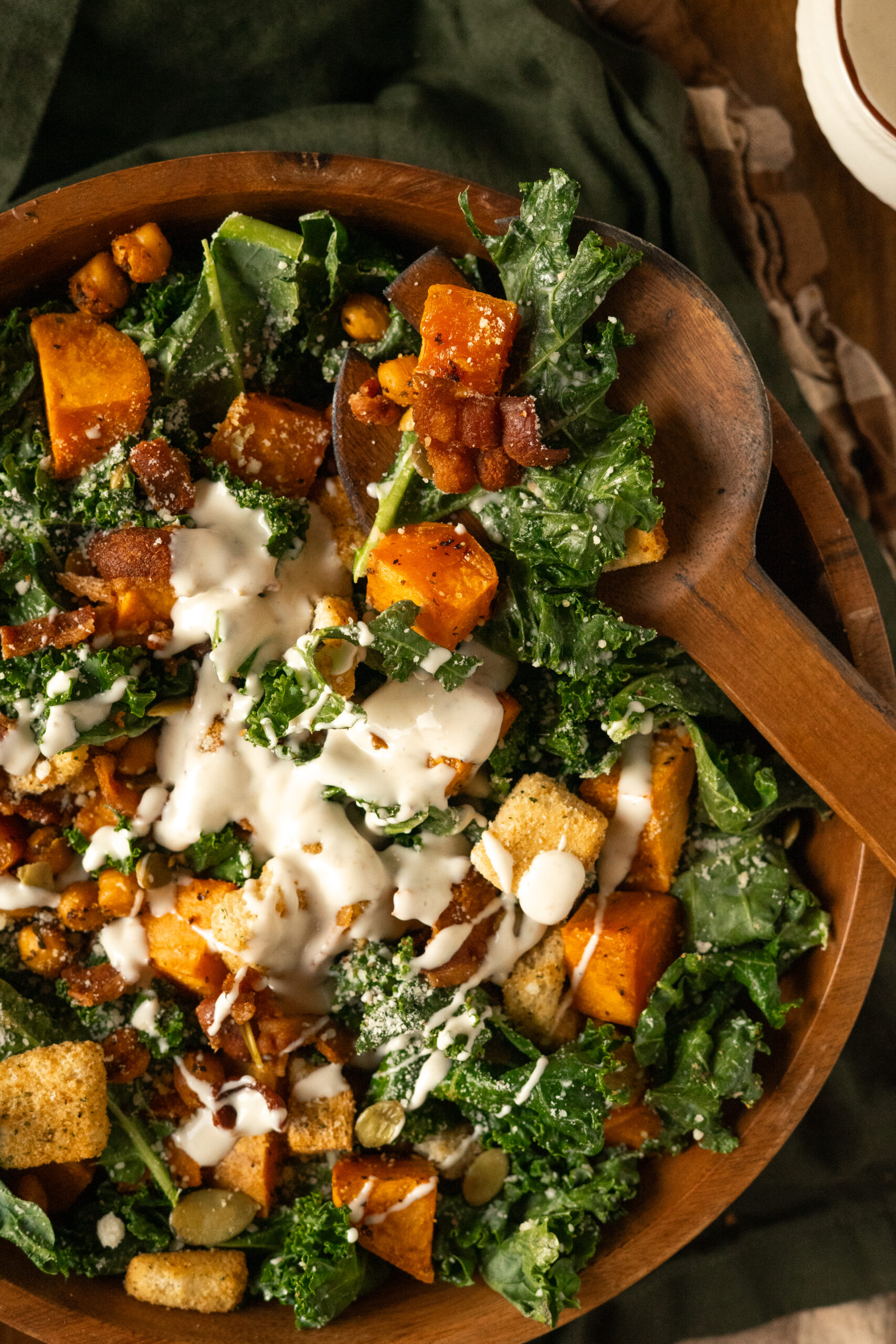 kale caesar salad in wooden bowl with wooden spoon on side.