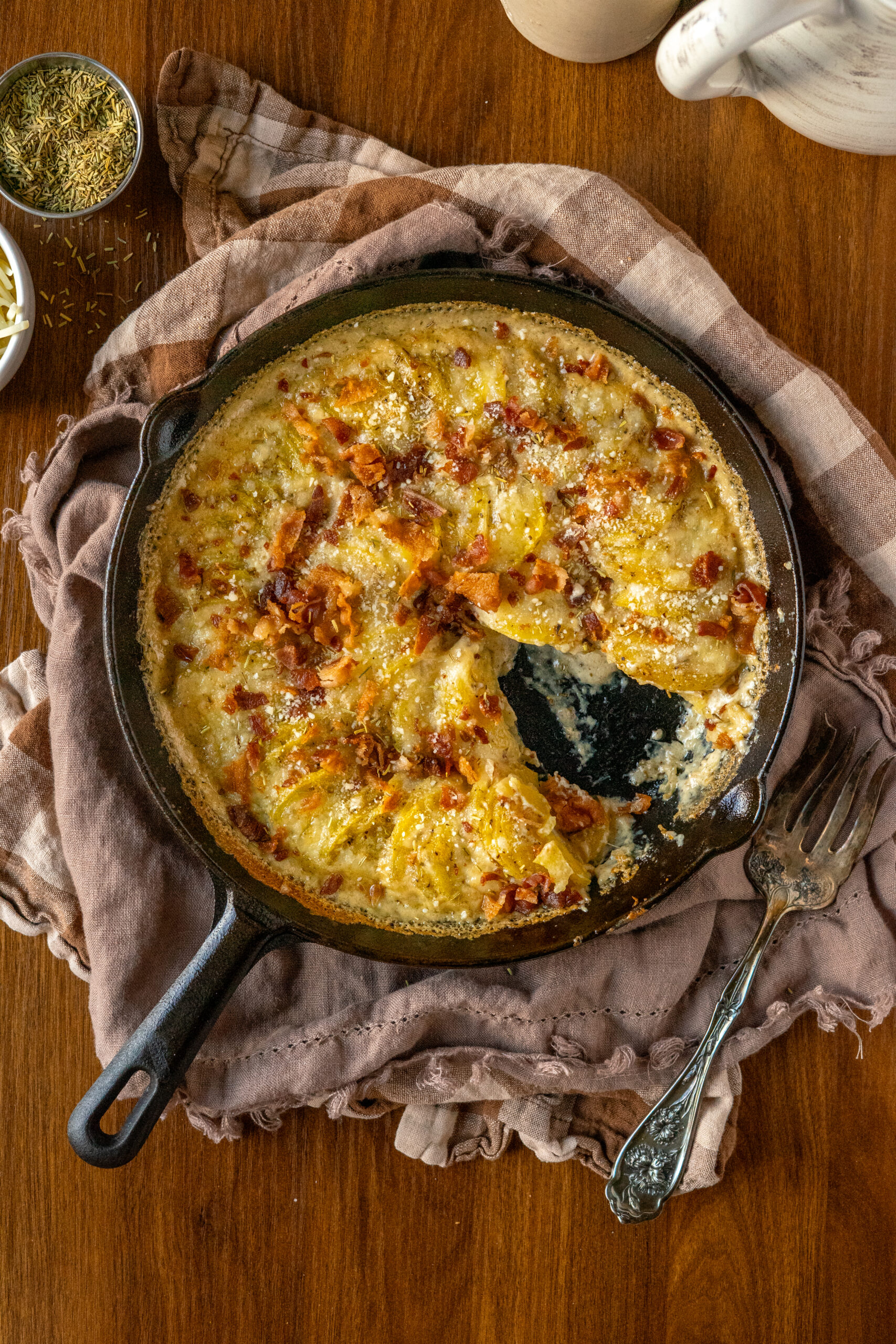 overhead view of potatoes au gratin in a cast iron pan on a wooden surface.