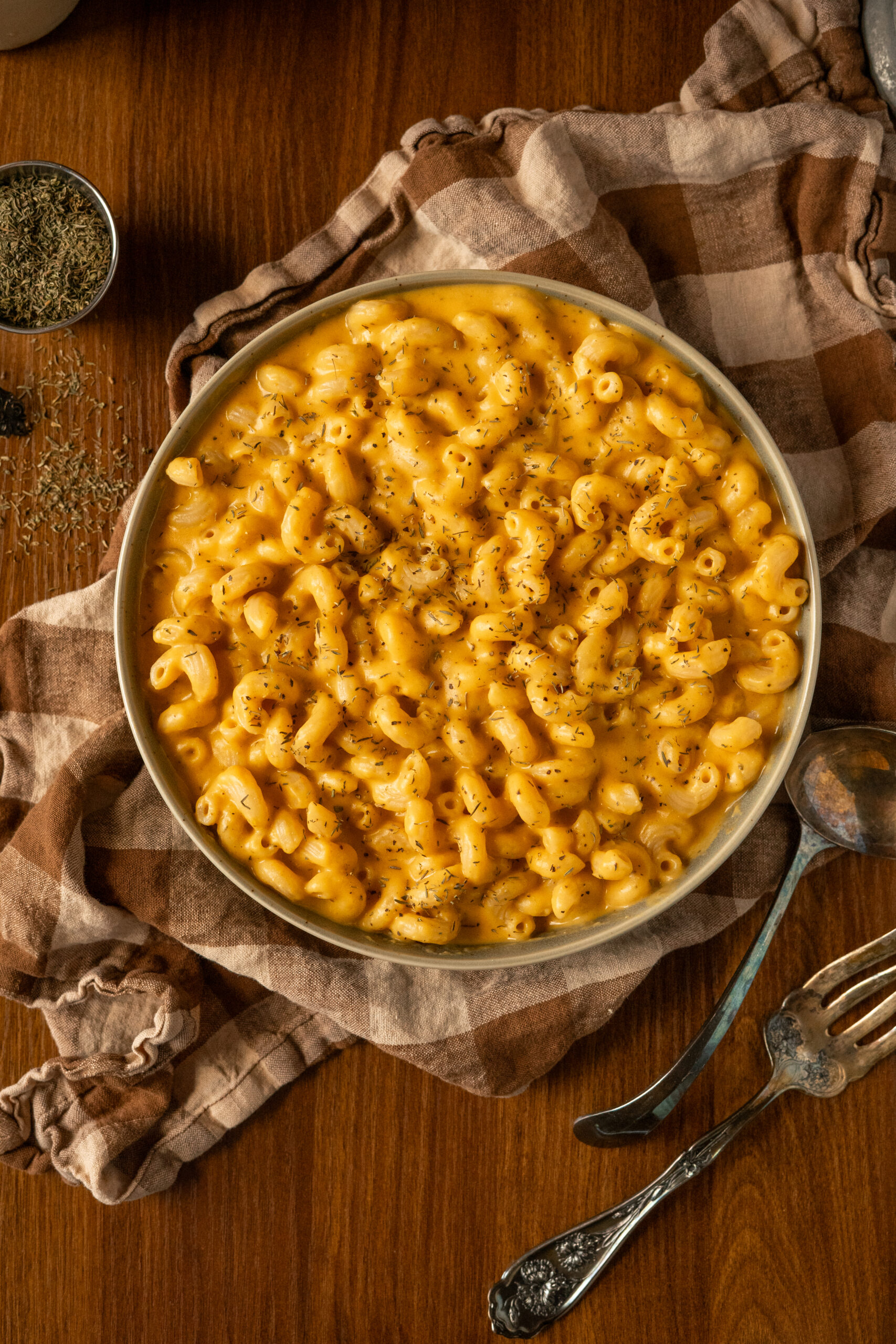 overhead view of mac and cheese in green bowl on wooden table with a brown checkered napkin.