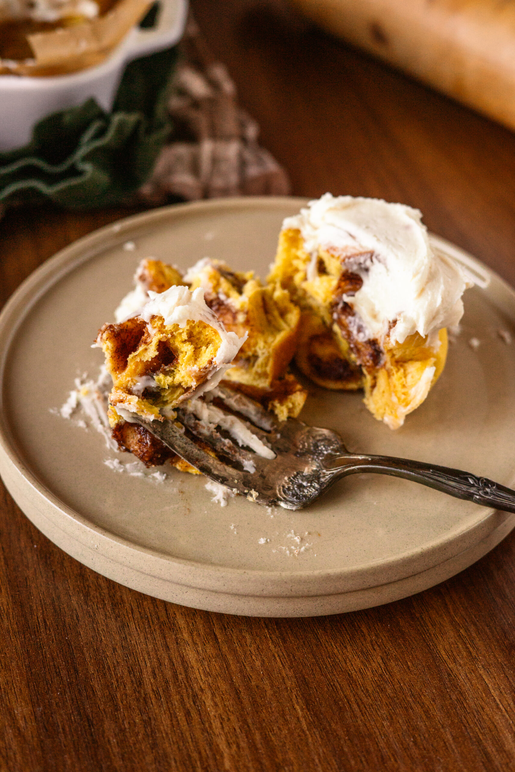 pumpkin cinnamon roll on a brown plate cut in half by a vintage fork.