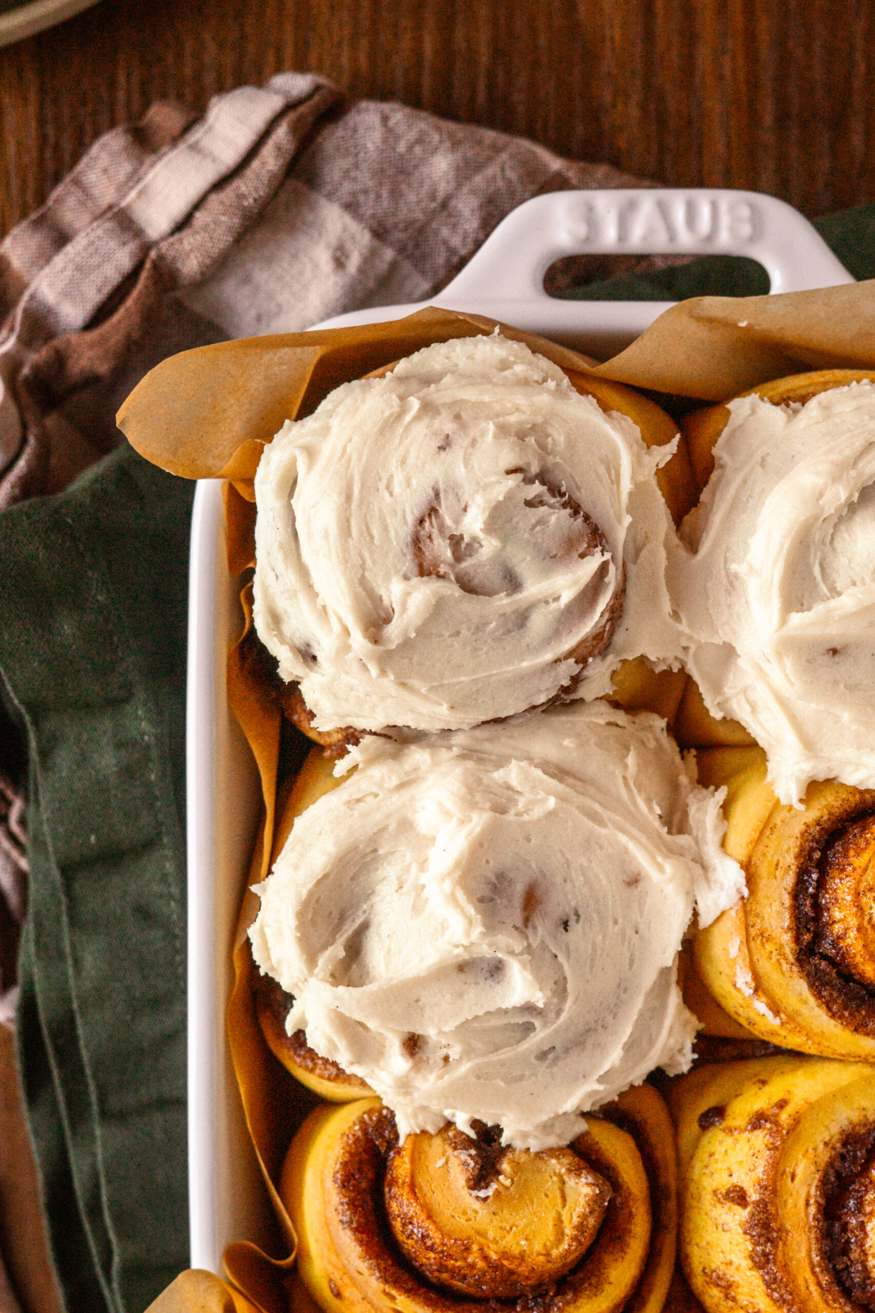 close up of pumpkin cinnamon rolls in a white pan with frosting on top.