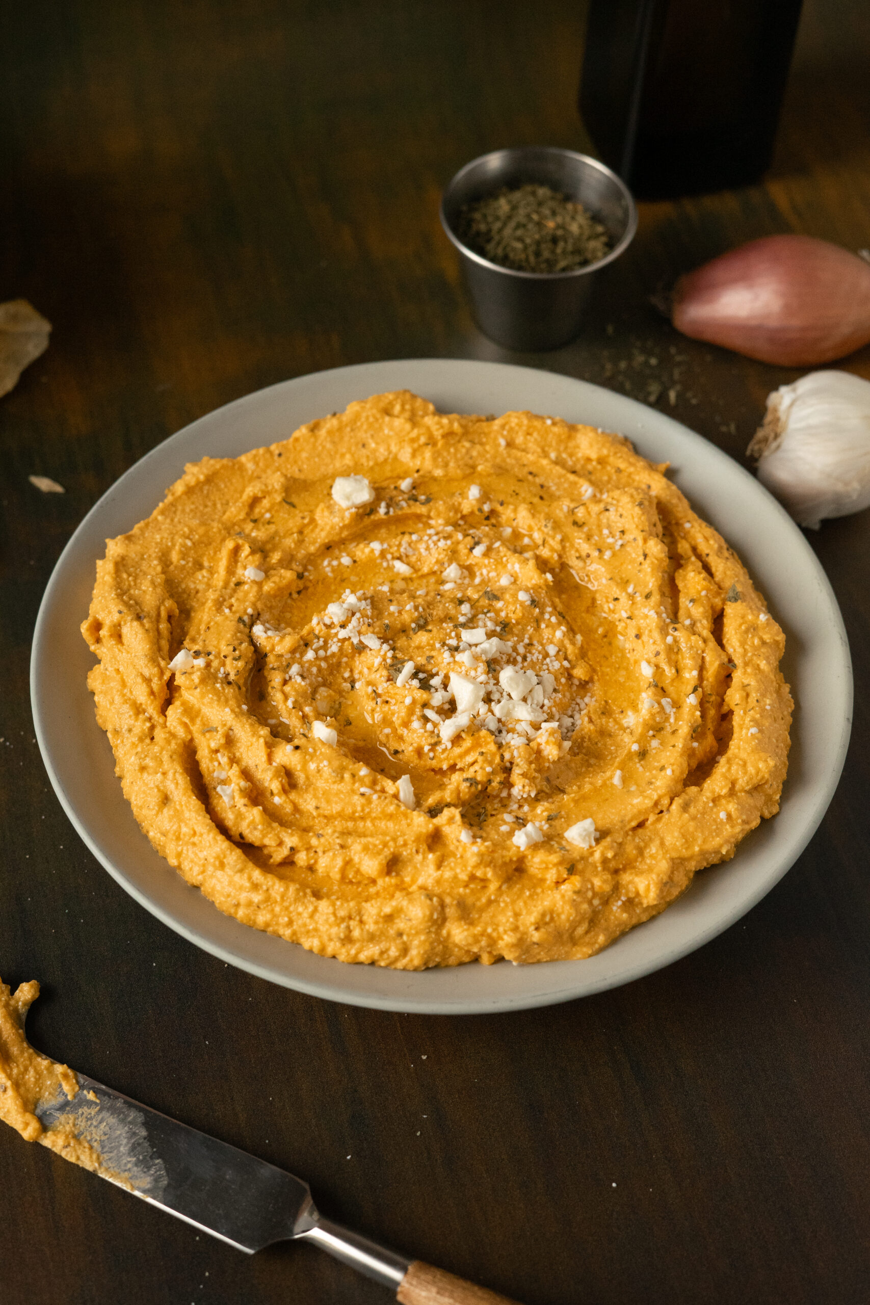 close up of pumpkin feta dip in a beige bowl on green surface.