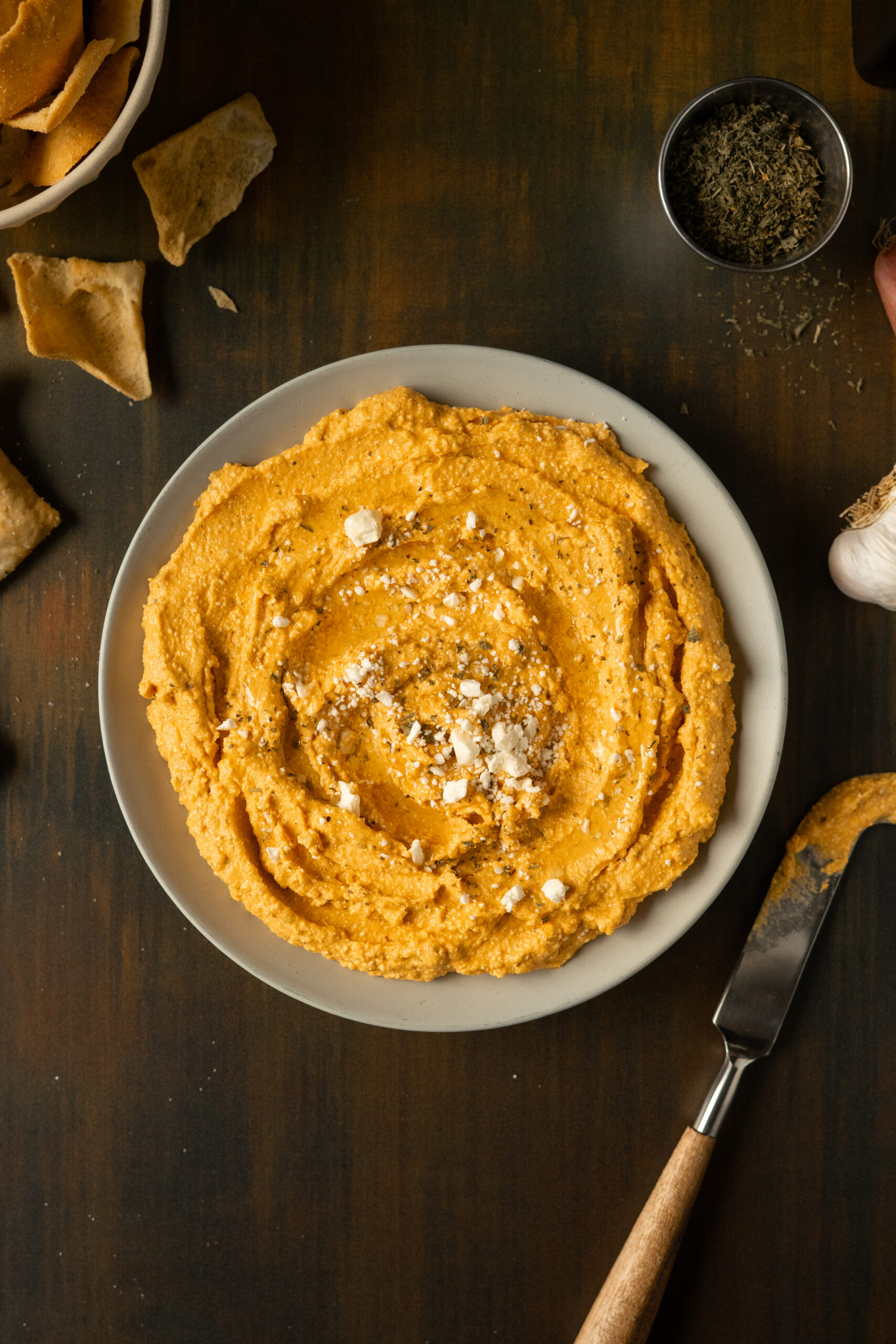 overhead view of pumpkin feta dip in a beige bowl on green surface.