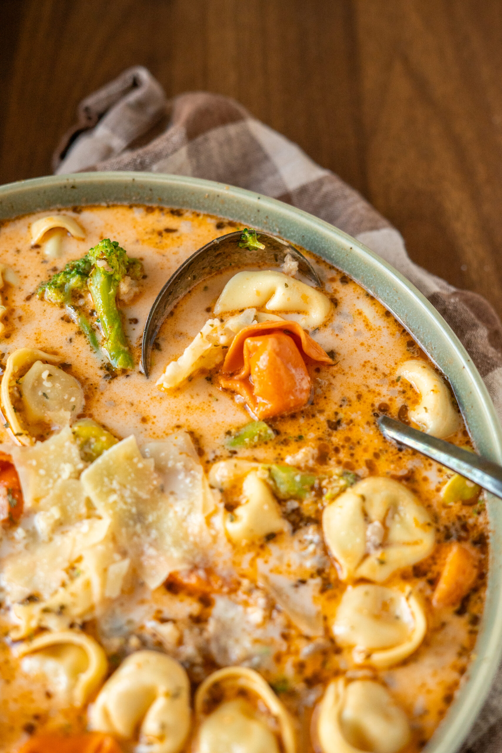 close up of tortellini soup with spoon in the bowl.