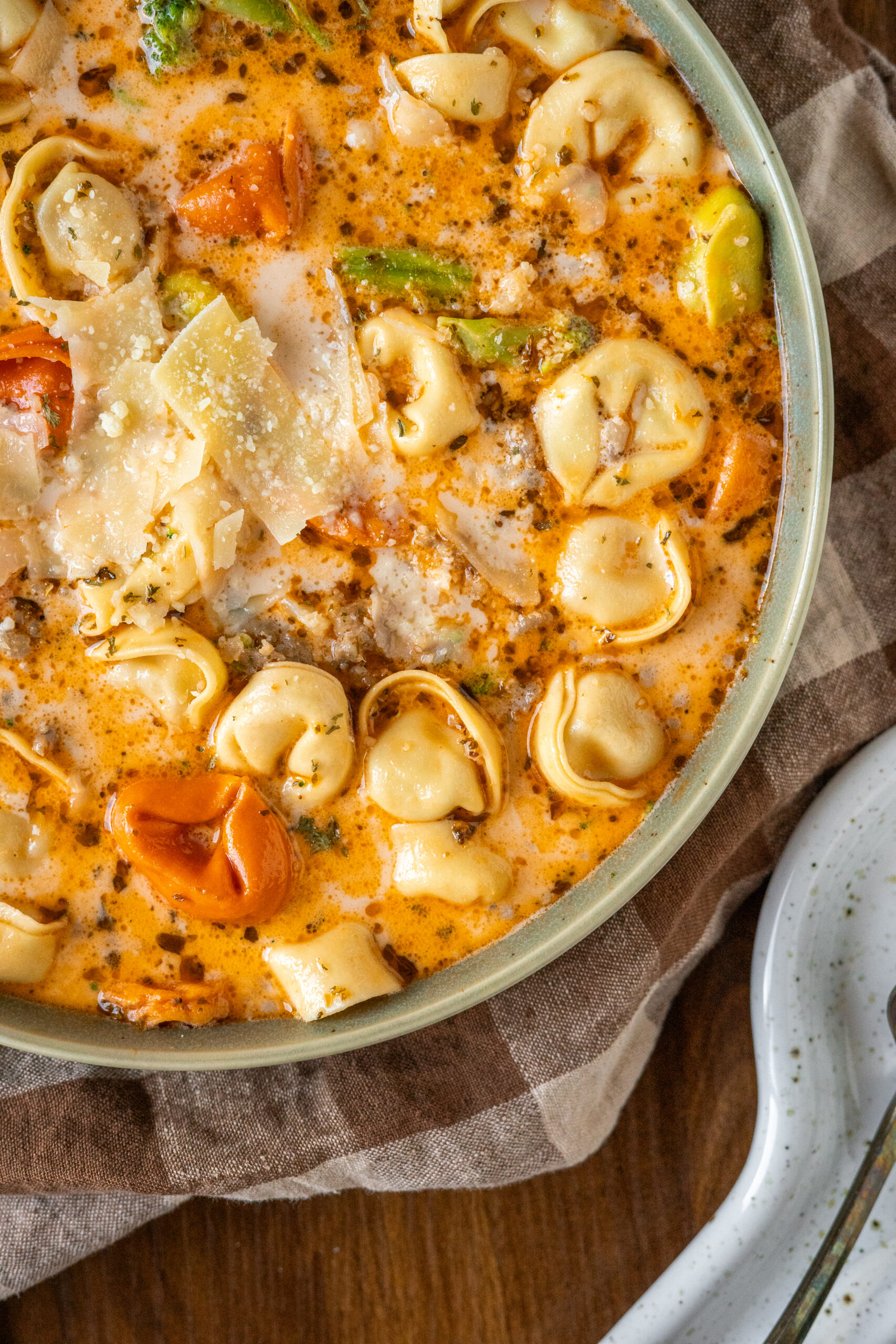 close up of tortellini soup with parmesan cheese on top.