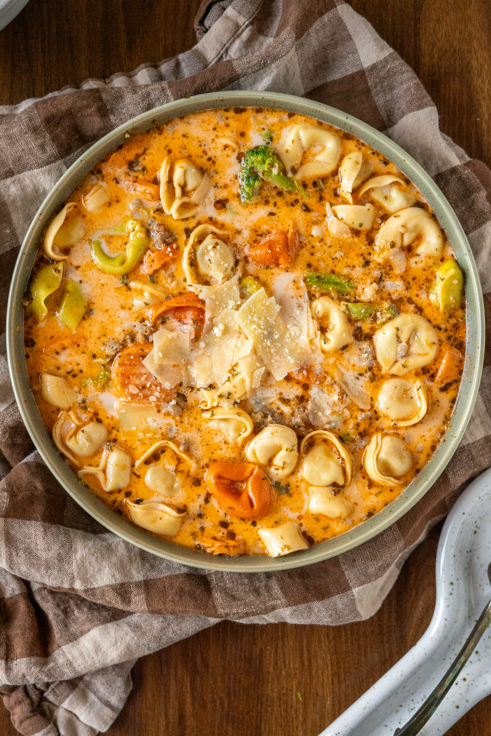 overhead shot of large bowl of tortellini soup on checkered napkin.