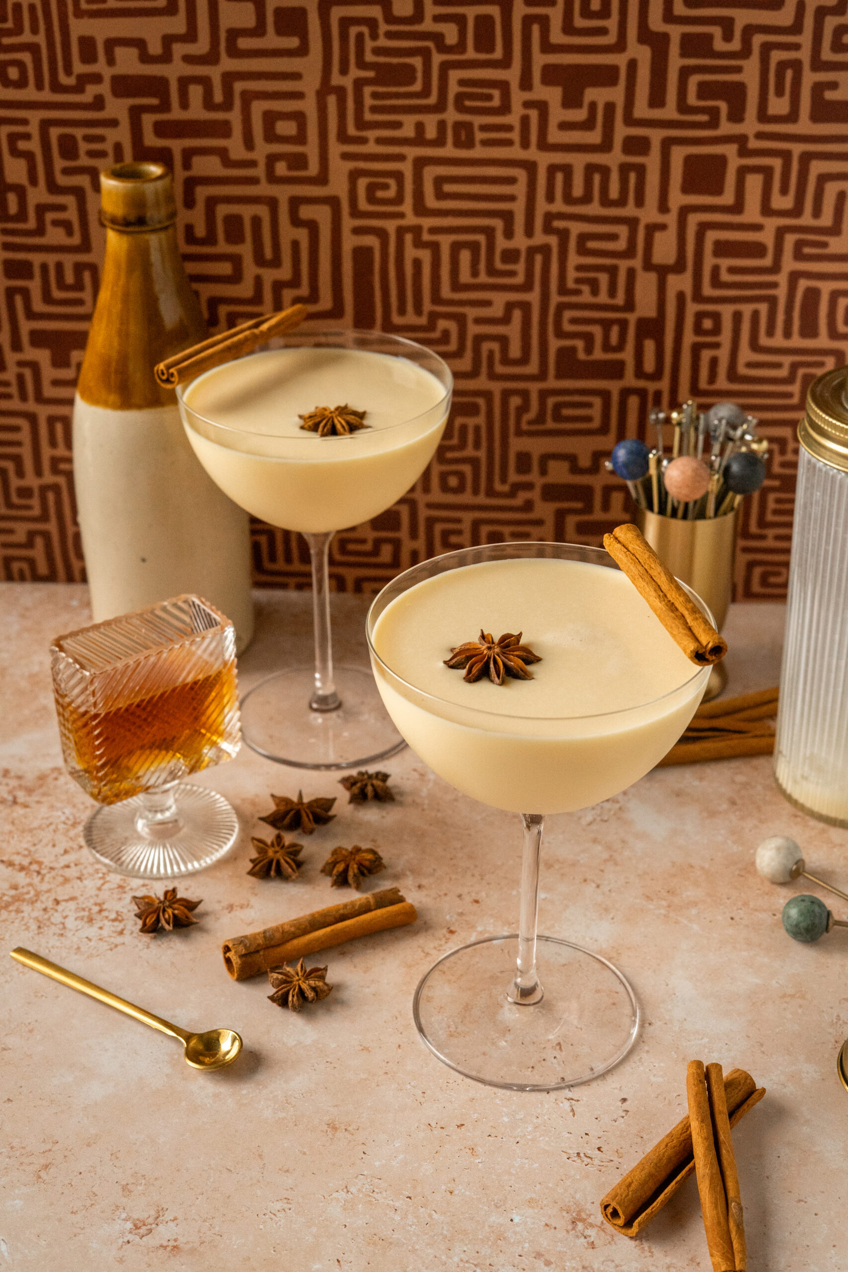 two eggnog martinis in coupe glasses in front of funky brown backdrop.