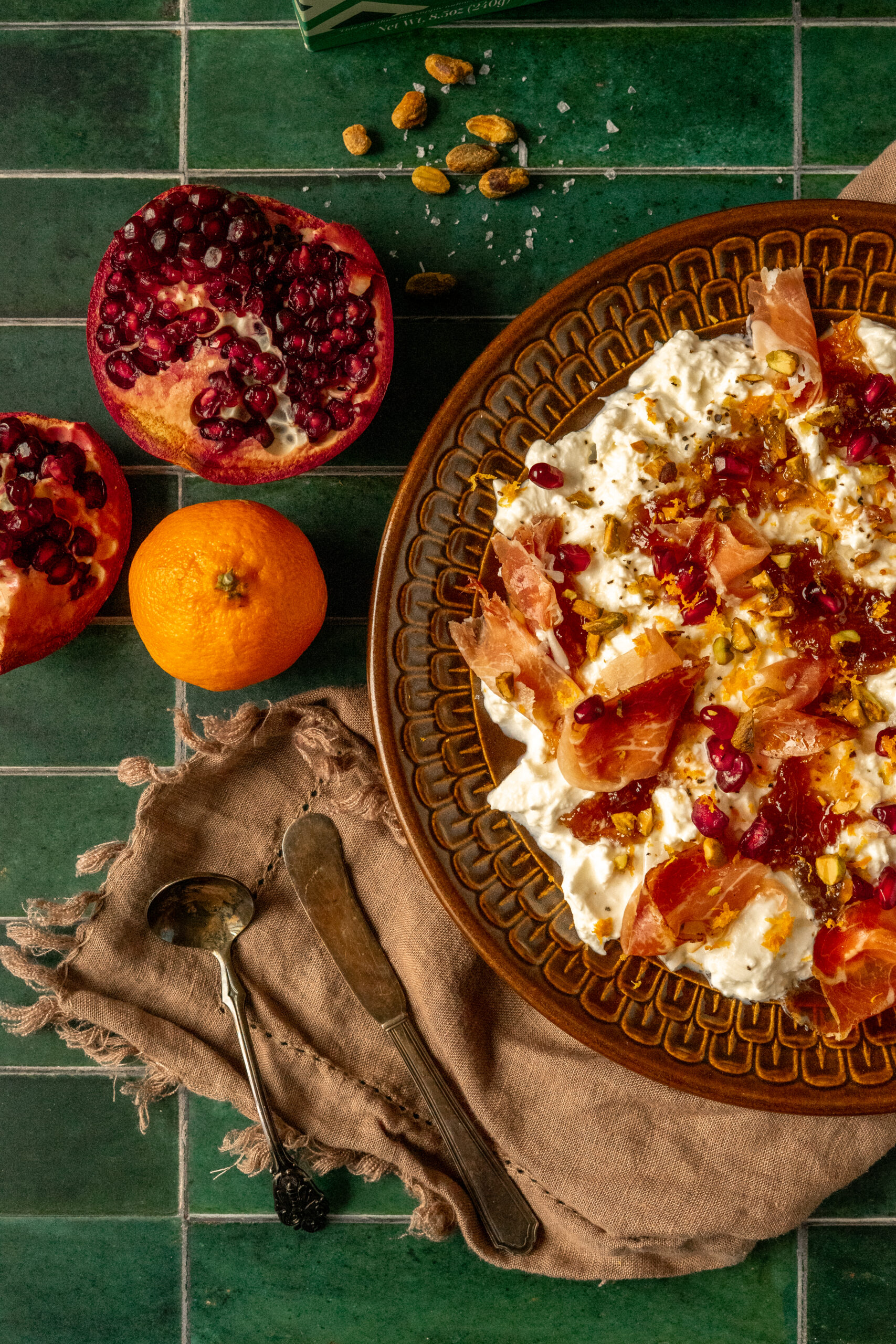 burrata plate on green tile background with pomegranate and orange in frame.