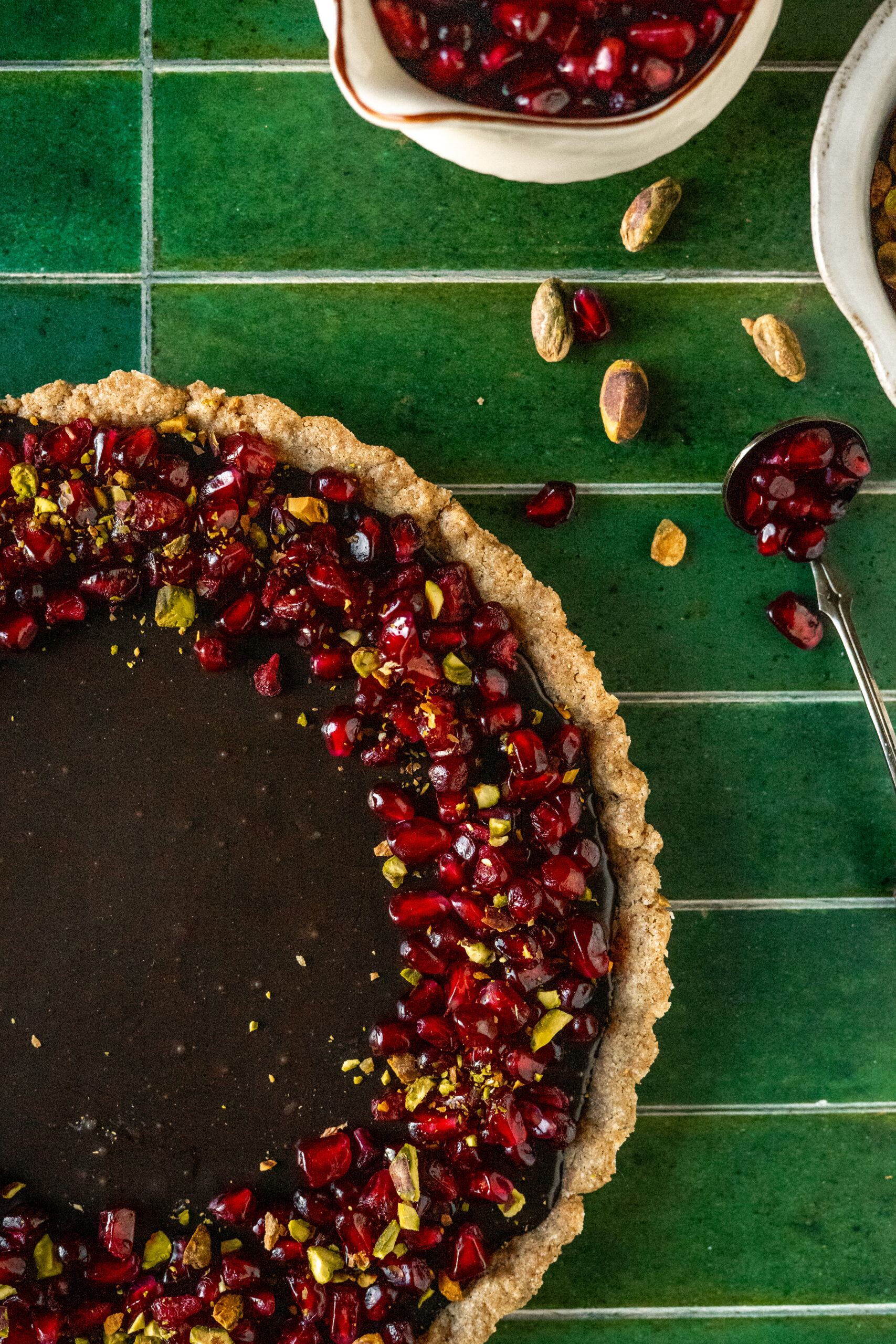 chocolate pomegranate tart on green tile surface.