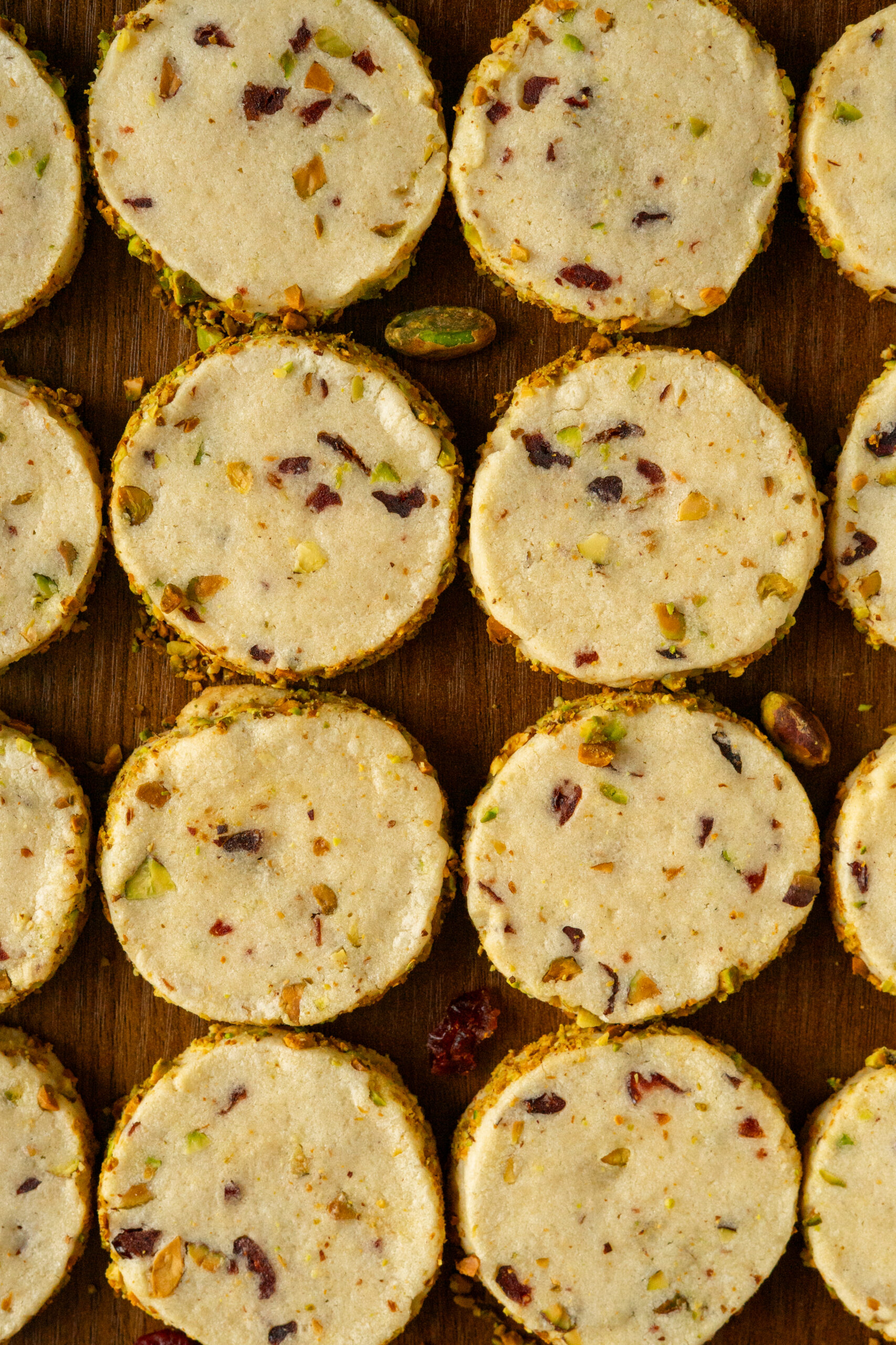 pistachio cranberry cookies arranged in lines on wooden table.