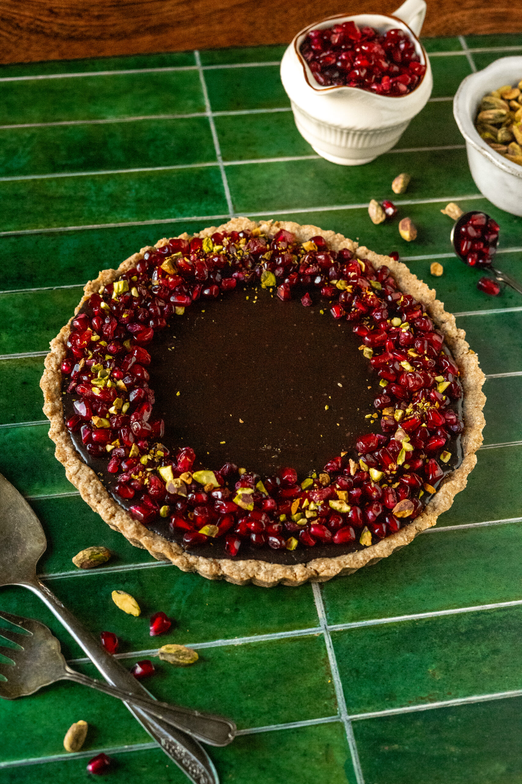 chocolate pomegranate tart on green tile surface.