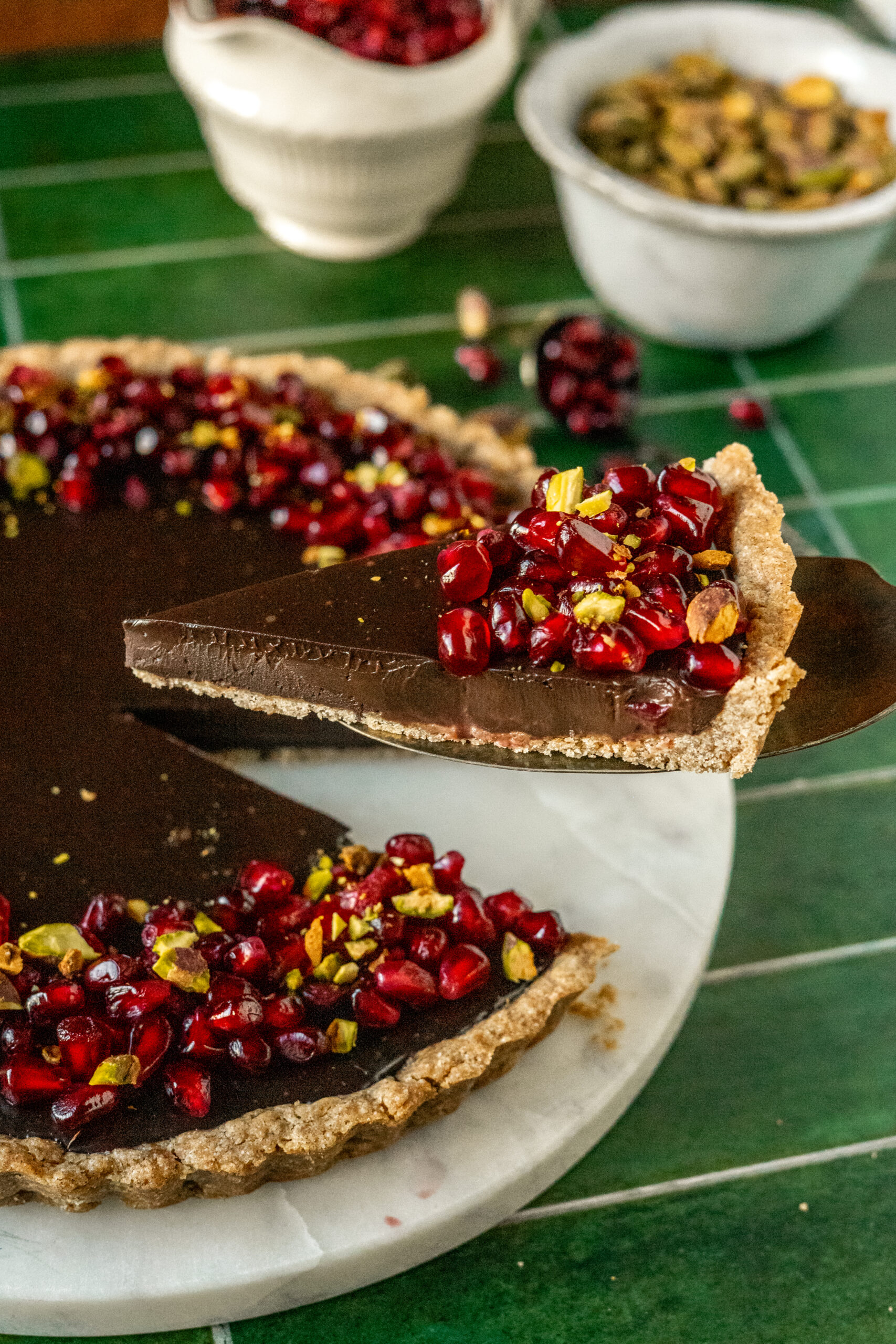 slice of chocolate pomegranate tart on serving knife held above tart.