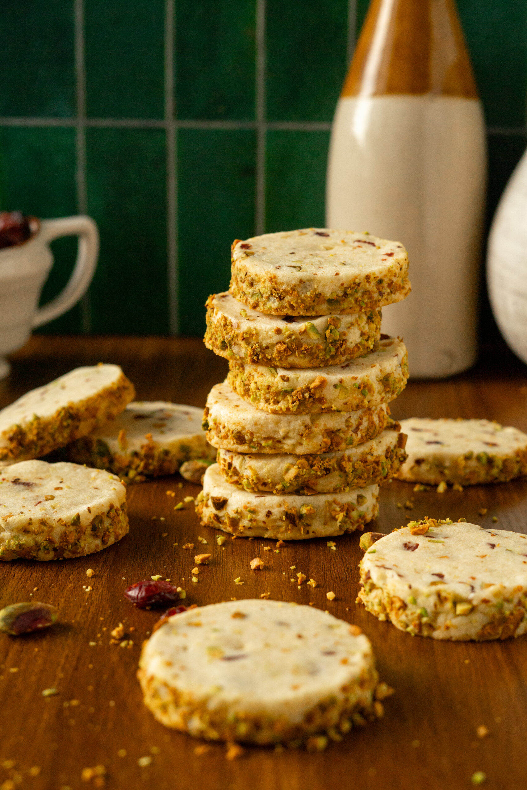 pistachio cranberry cookies stacked on wooden table with green background.