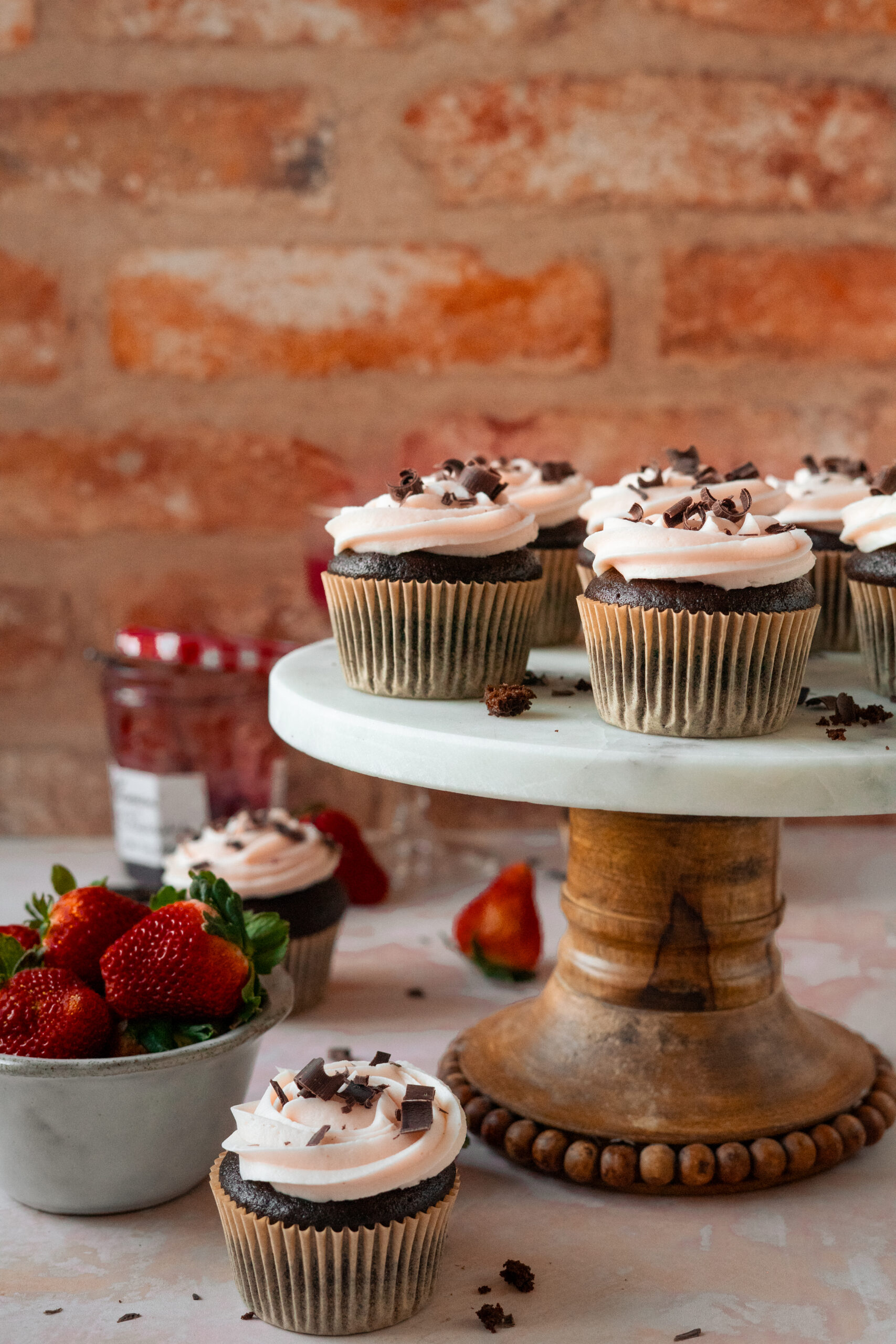 chocolate strawberry cupcakes on a marble cake stand with brick wall in background.